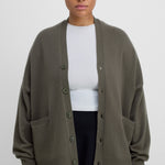 man wearing an oversized army green cashmere v-neck cardigan with five corozo buttons and two front pockets.