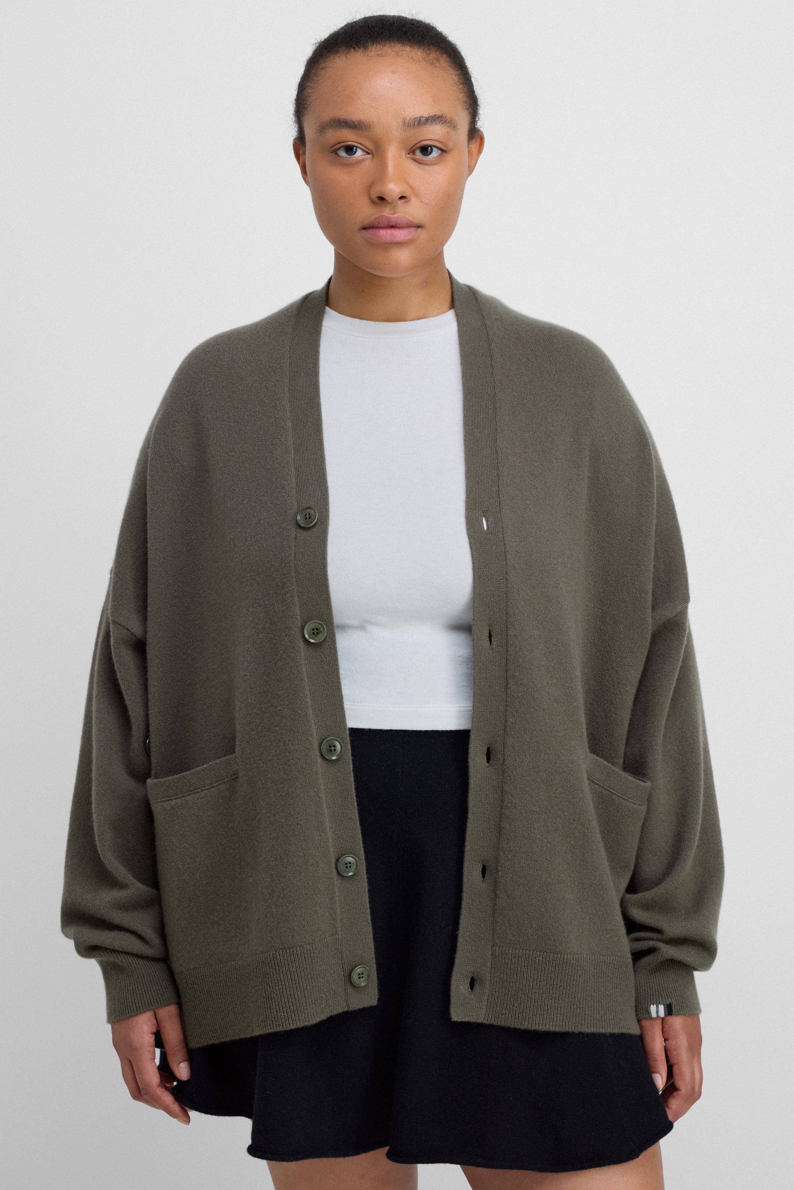 man wearing an oversized army green cashmere v-neck cardigan with five corozo buttons and two front pockets.