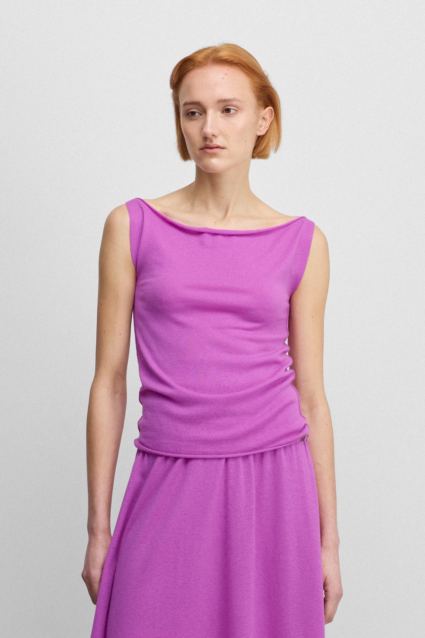 woman wearing a bright pink sleeveless wool cashmere top with a boat neck, styled with a matching pink skirt.