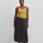 woman wearing a slightly sheer dark grey wool cashmere midi skirt, styled with a yellow top.