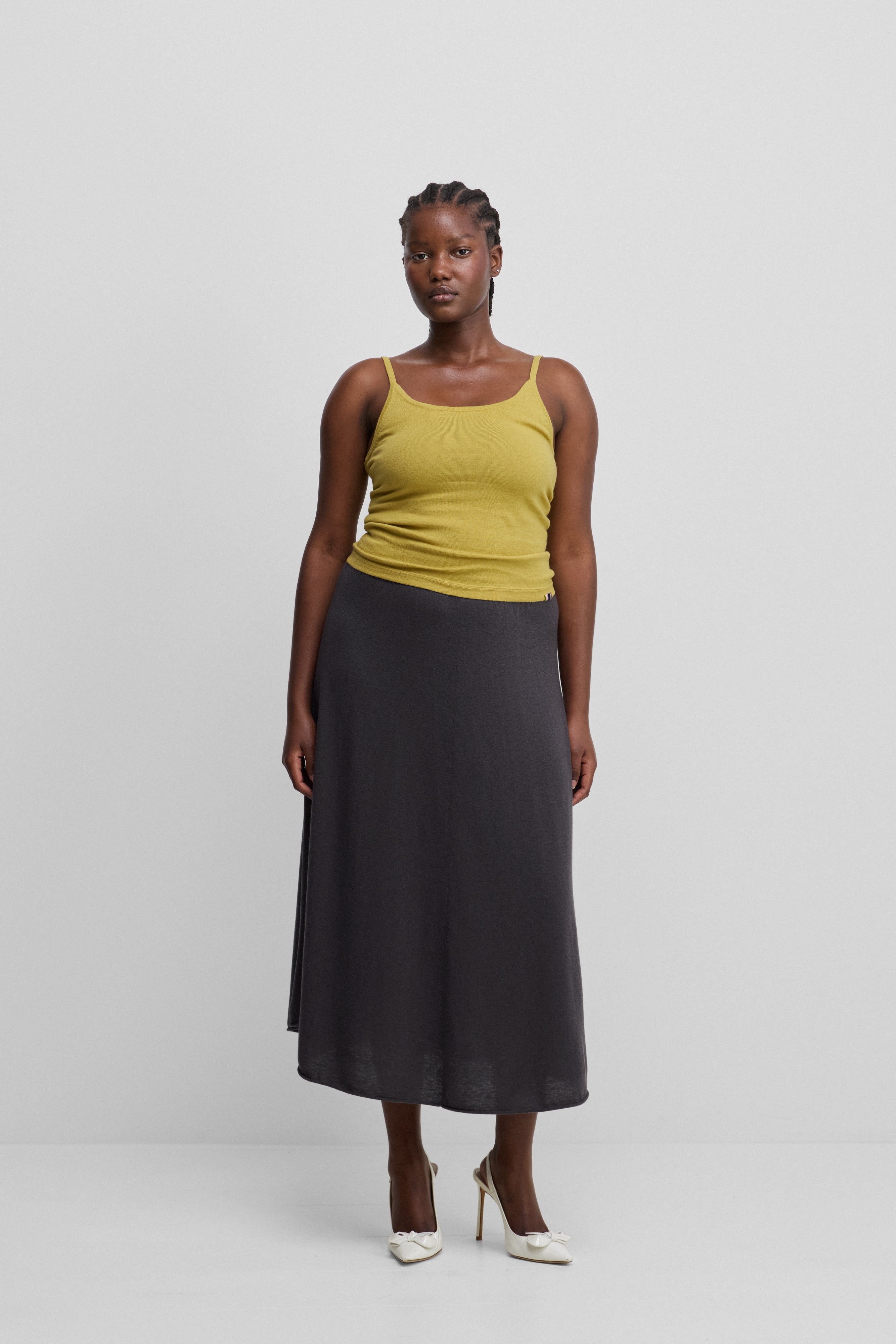 woman wearing a slightly sheer dark grey wool cashmere midi skirt, styled with a yellow top.