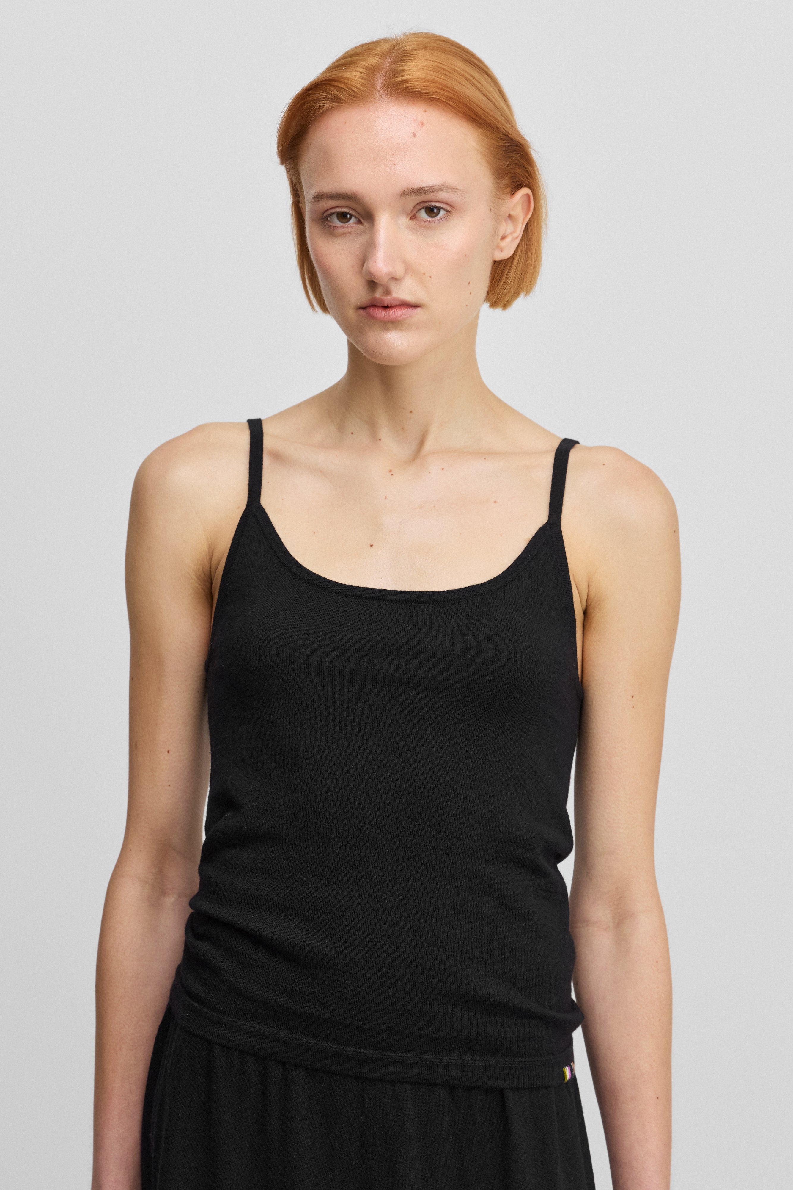 woman wearing a black fitted cotton cashmere strap top with a round neckline.