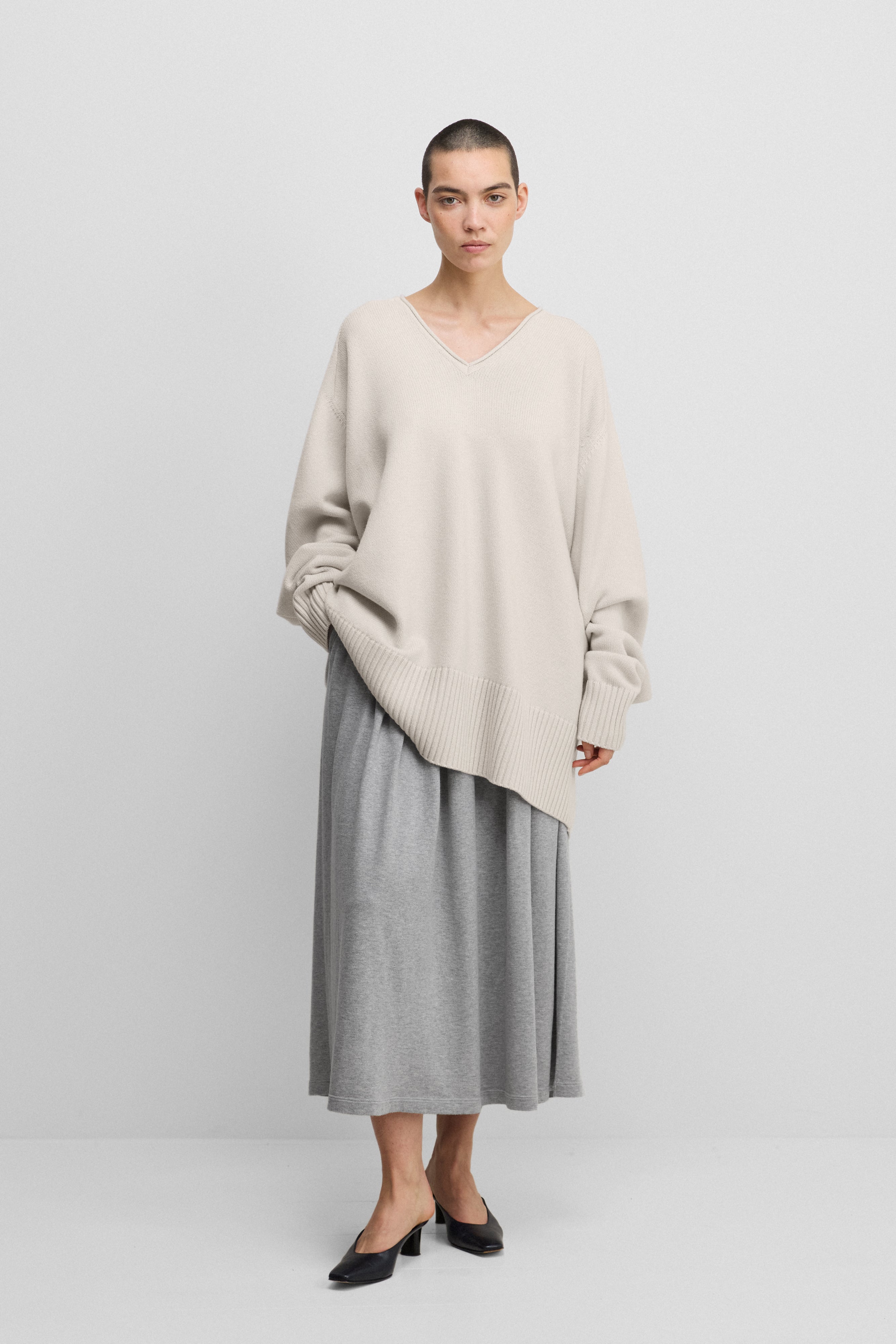 woman wearing a white oversized cashmere v-neck sweater with ribbed hem and cuffs, styled with a skirt.