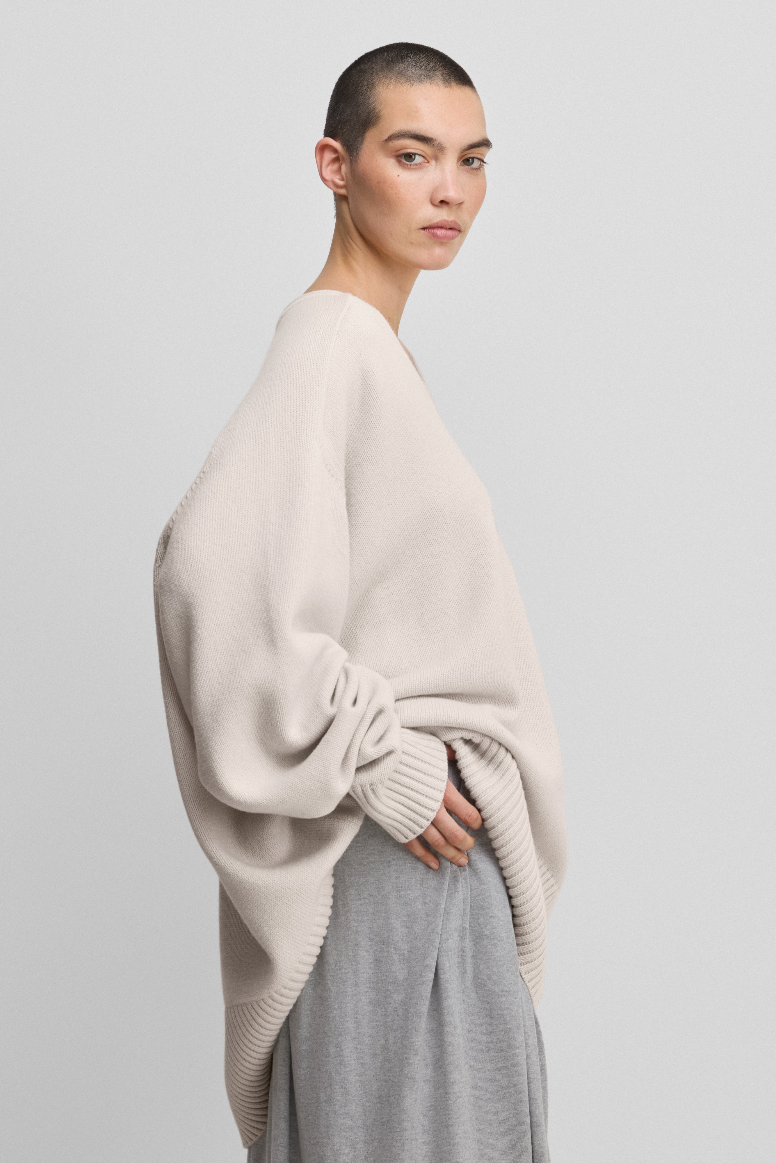woman wearing a white oversized cashmere v-neck sweater with ribbed trims and extra long sleeves, shown from the side.