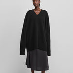 woman wearing a black oversized cashmere v-neck sweater with ribbed hem and cuffs and extra long sleeves.