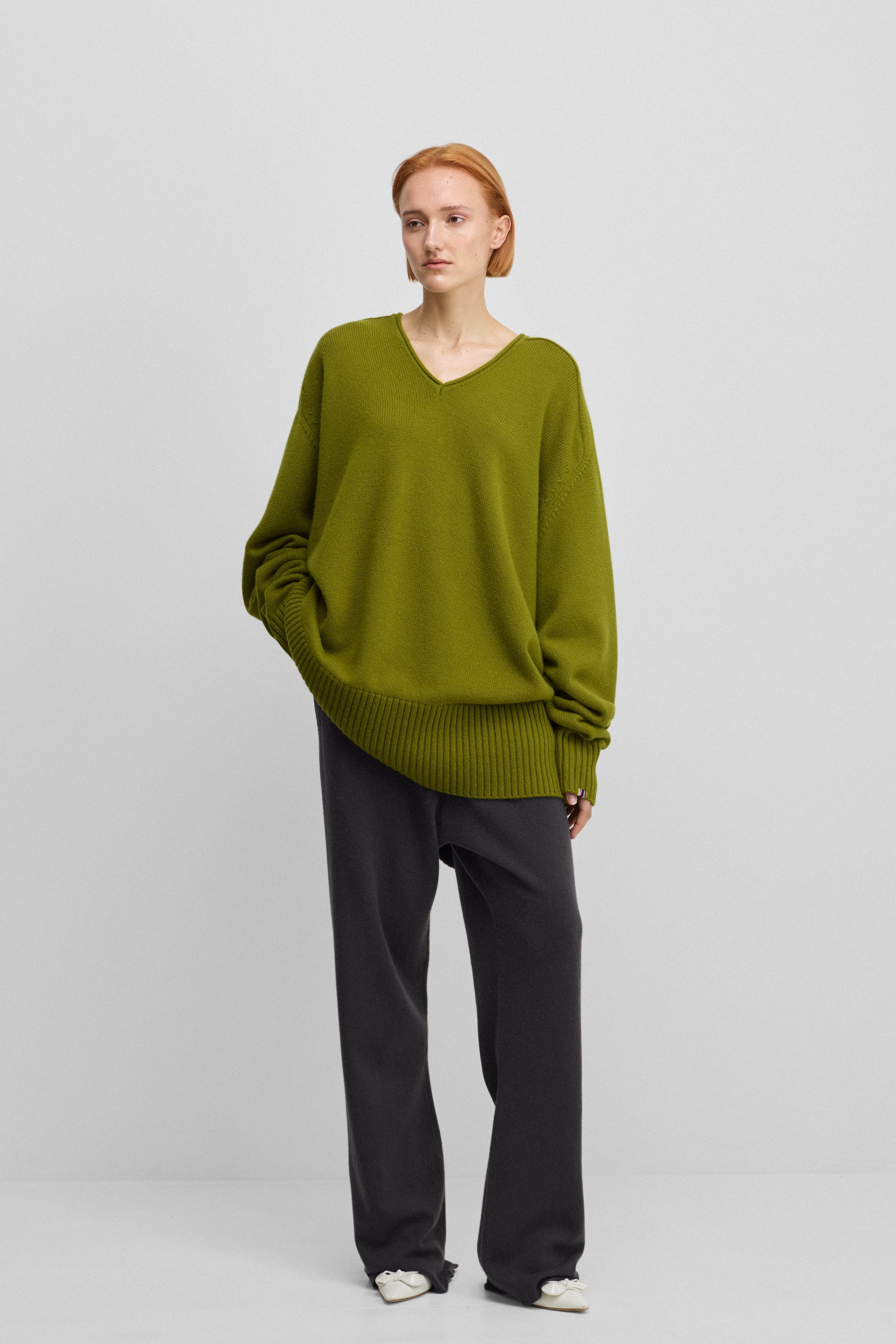 woman wearing a green oversized cashmere v-neck sweater with ribbed hem and cuffs and extra long sleeves.