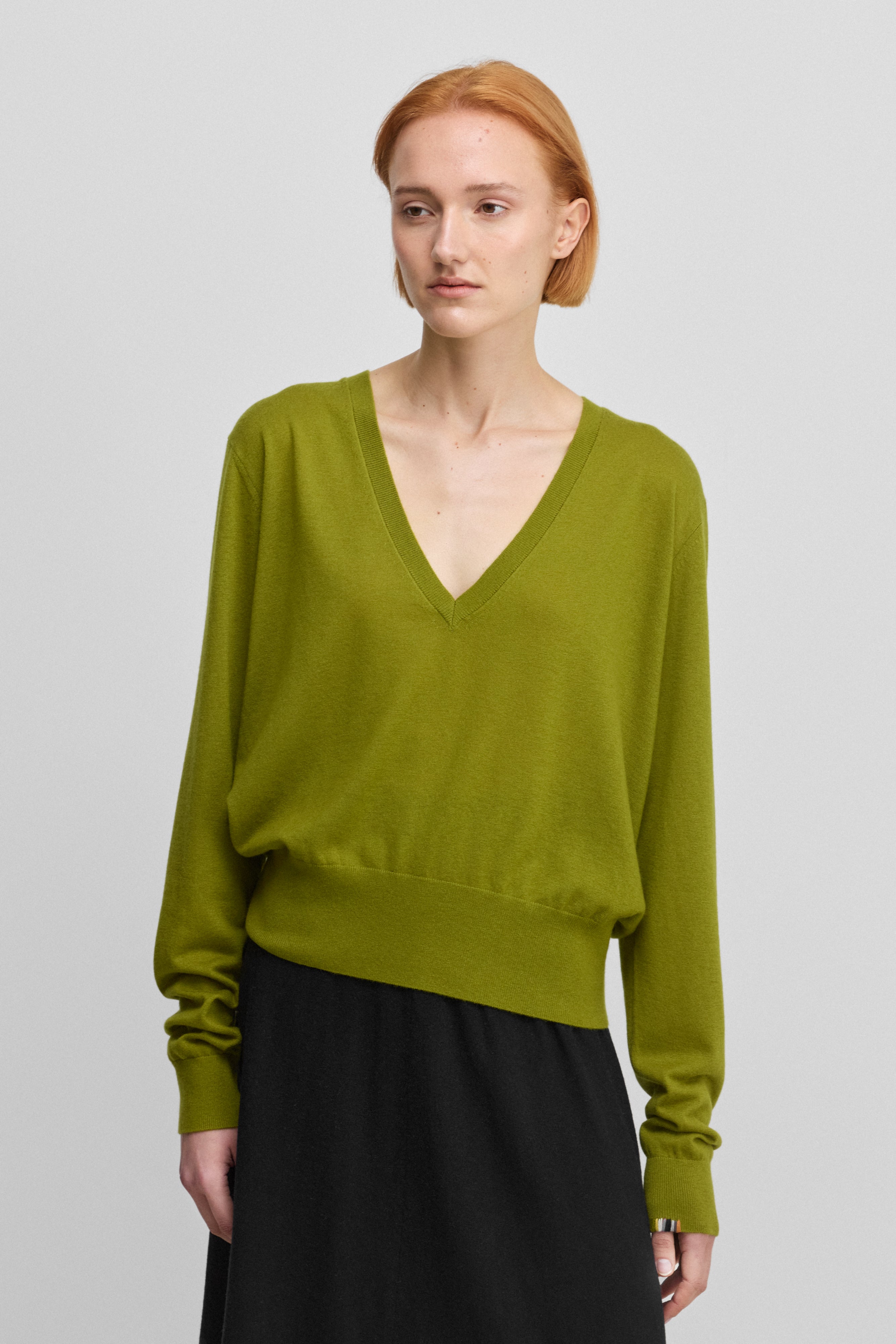 woman wearing a loose-fit green wool cashmere v-neck sweater with ribbed hem and cuffs.