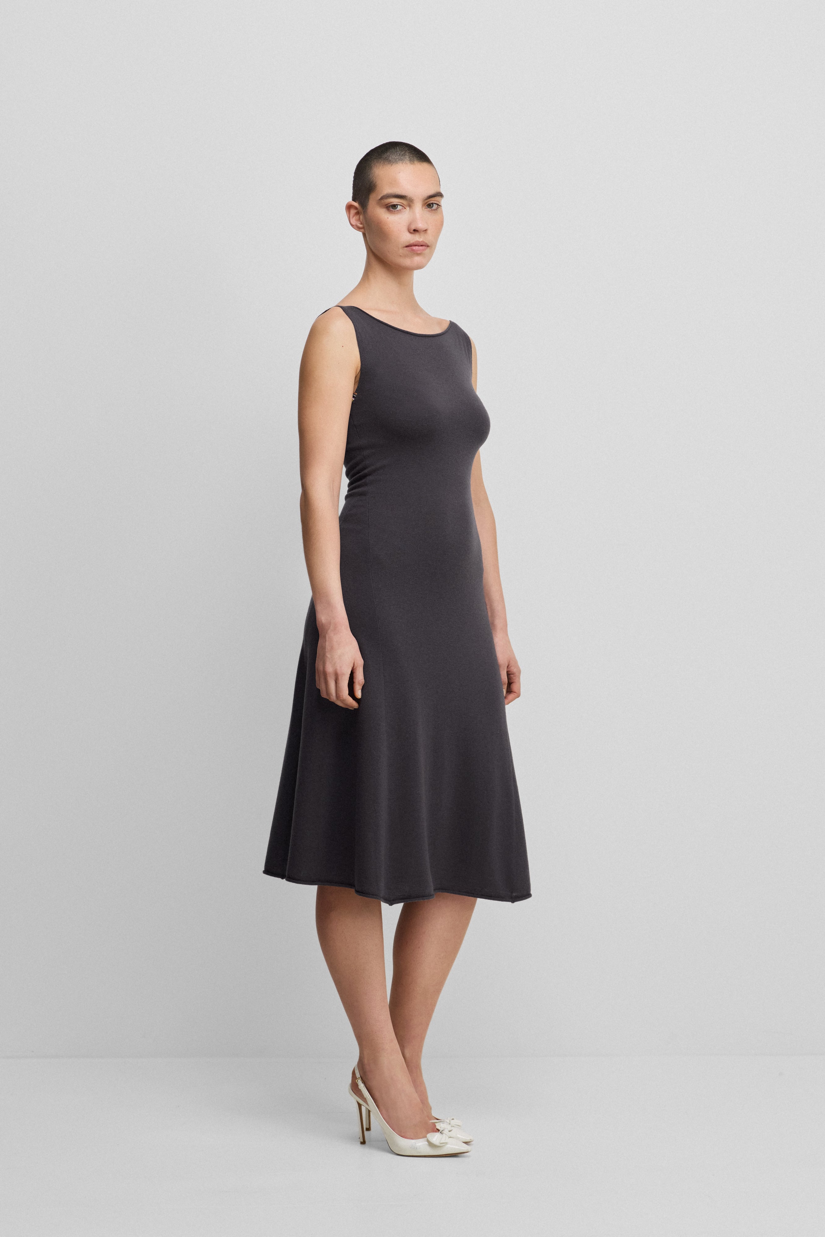 woman wearing a dark grey sleeveless wool cashmere a-line dress in midi length with a boat neckline.
