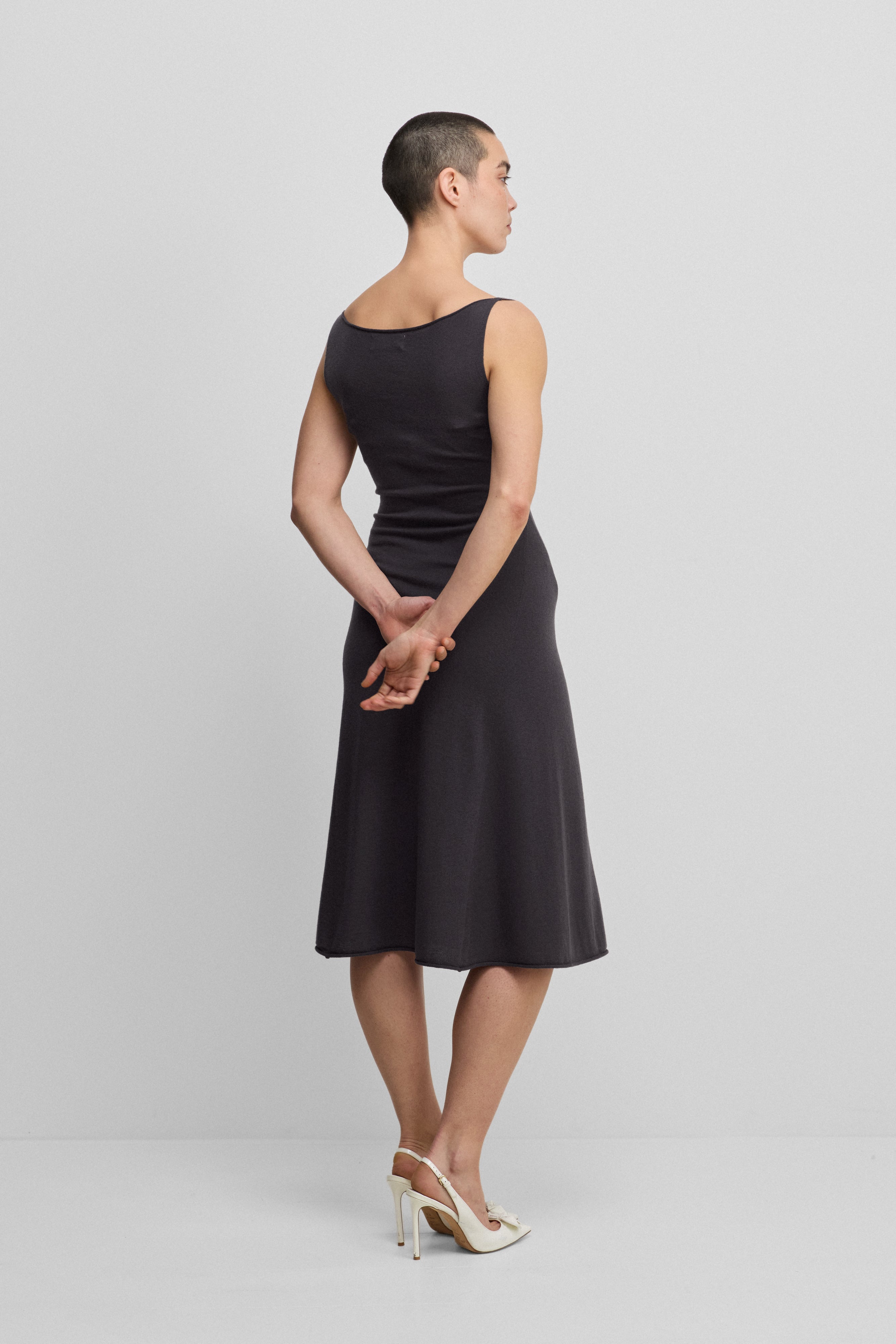 woman wearing a dark grey sleeveless wool cashmere a-line dress in midi length, shown from the back.