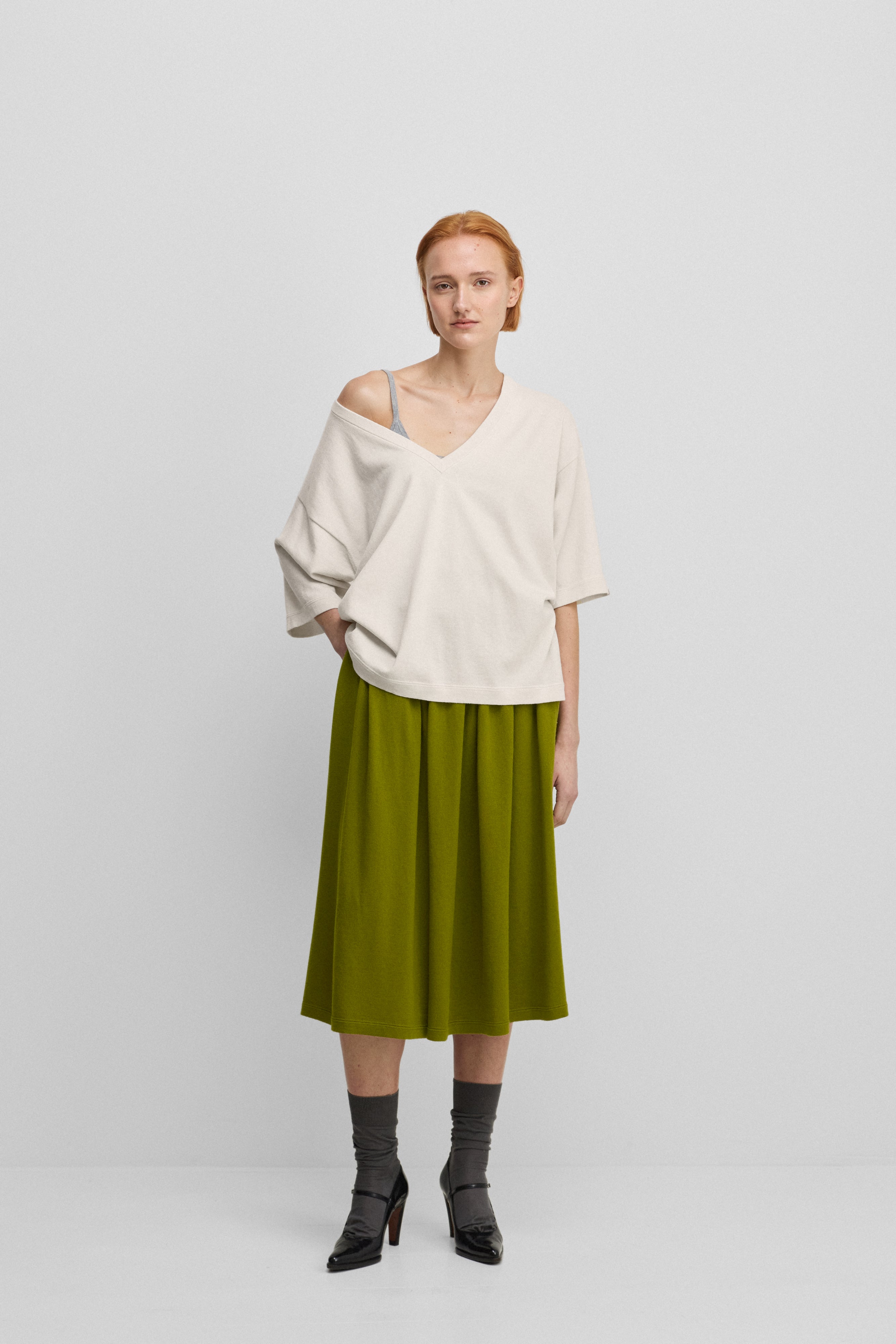 woman wearing a green cotton cashmere midi skirt with side pockets, styled with a white t-shirt.