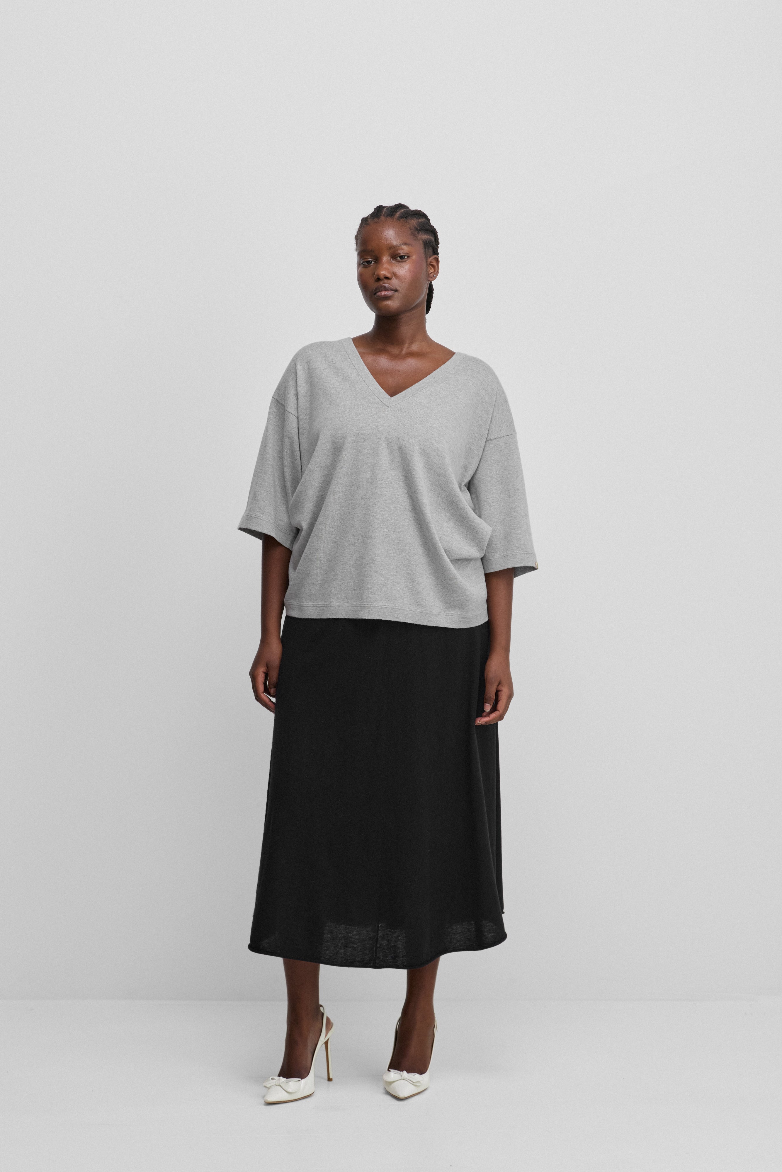 woman wearing a loose-fit grey cotton cashmere v-neck t-shirt with elbow-length sleeves, styled with a skirt.