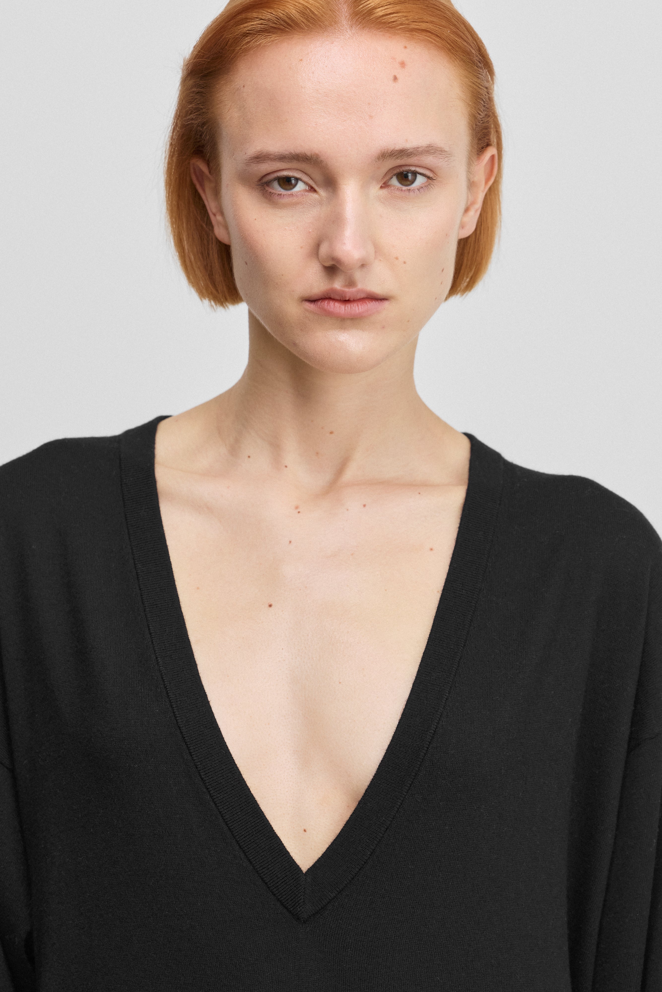 detail of a deep v-neckline of a black long-sleeved t-shirt dress in cotton cashmere.