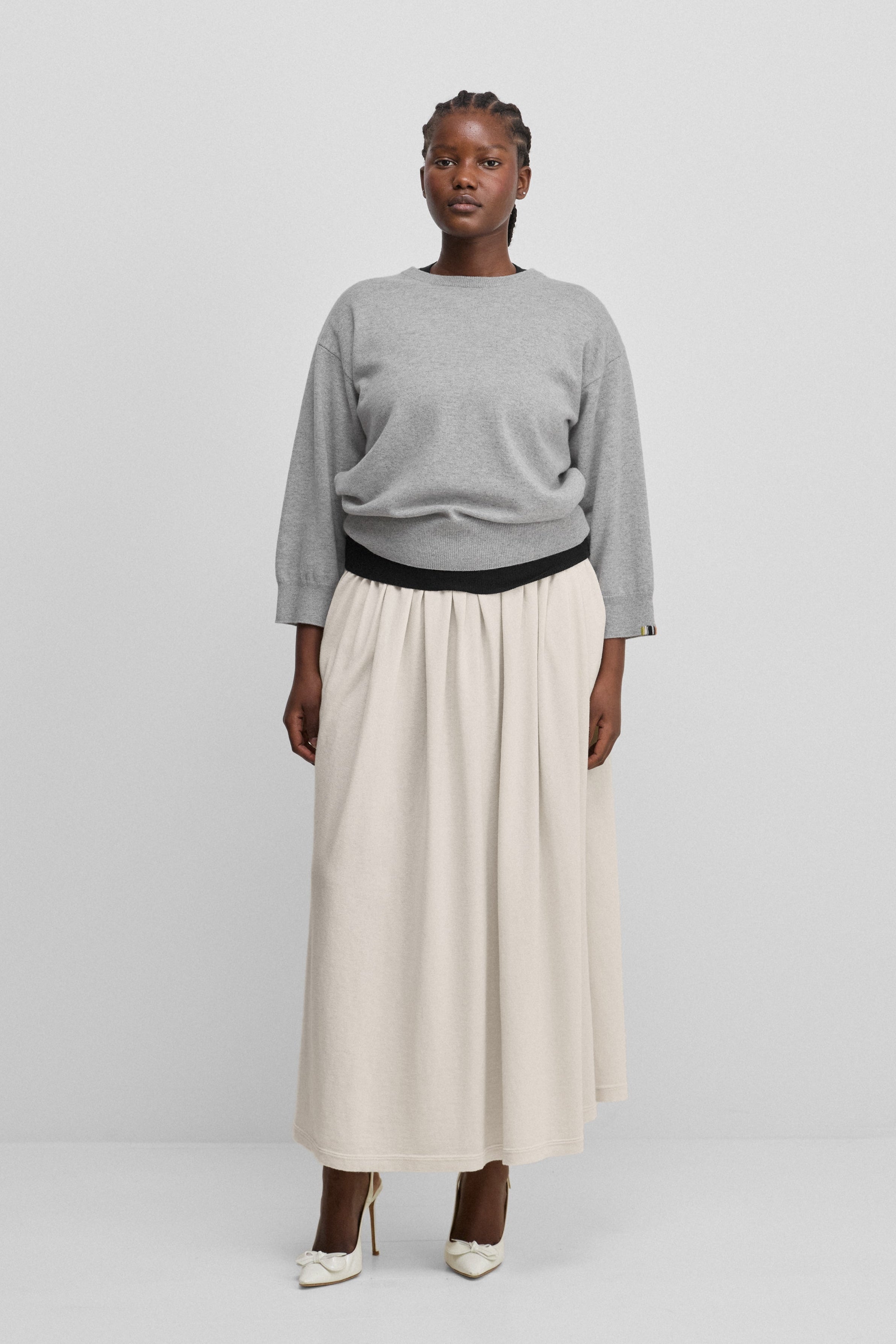 woman wearing a light grey 3/4-sleeve cashmere crewneck sweater, styled with a white skirt.
