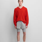 man wearing a bright red relaxed-fit cashmere v-neck sweater with ribbed trims, styled with grey shorts.