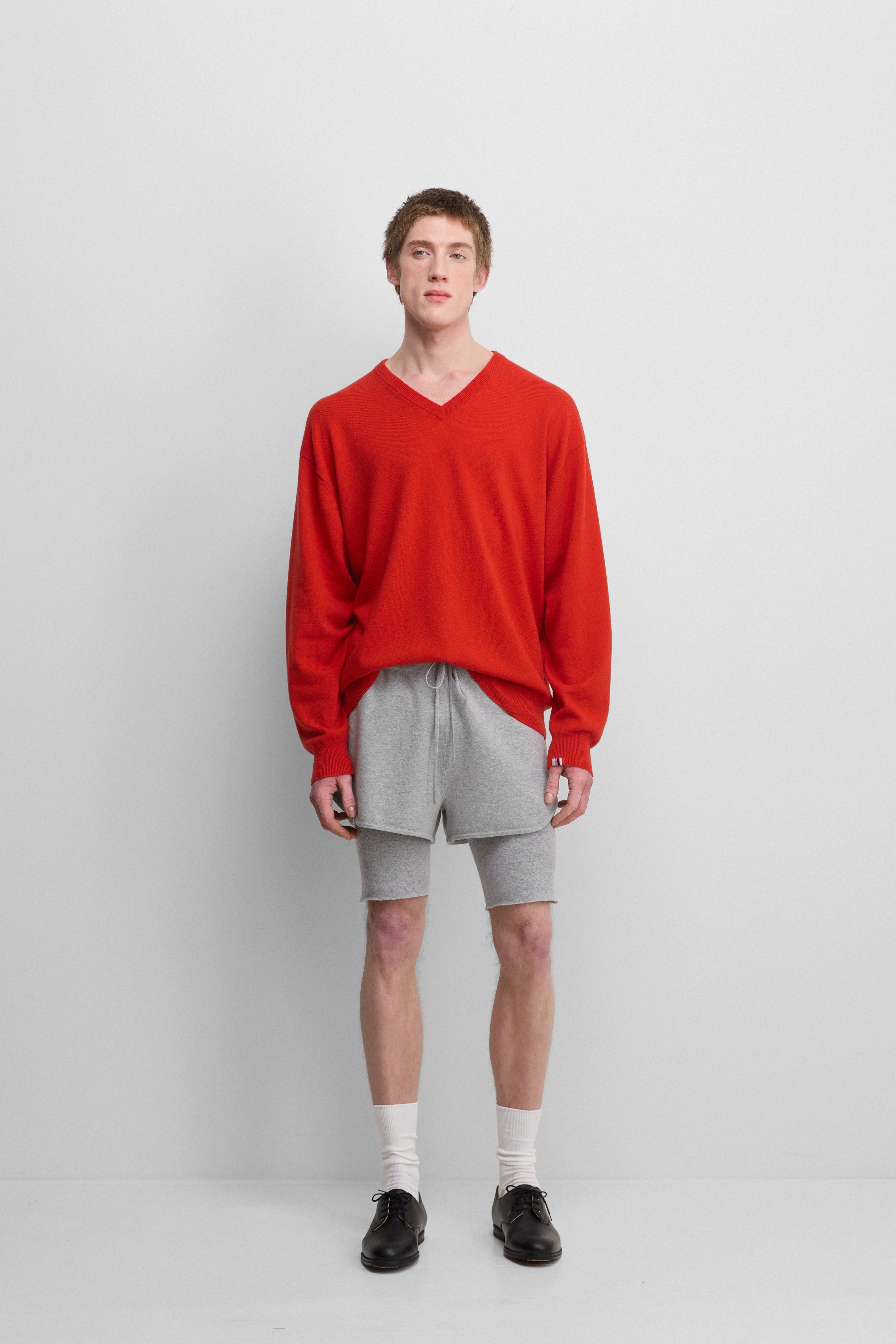 man wearing a bright red relaxed-fit cashmere v-neck sweater with ribbed trims, styled with grey shorts.