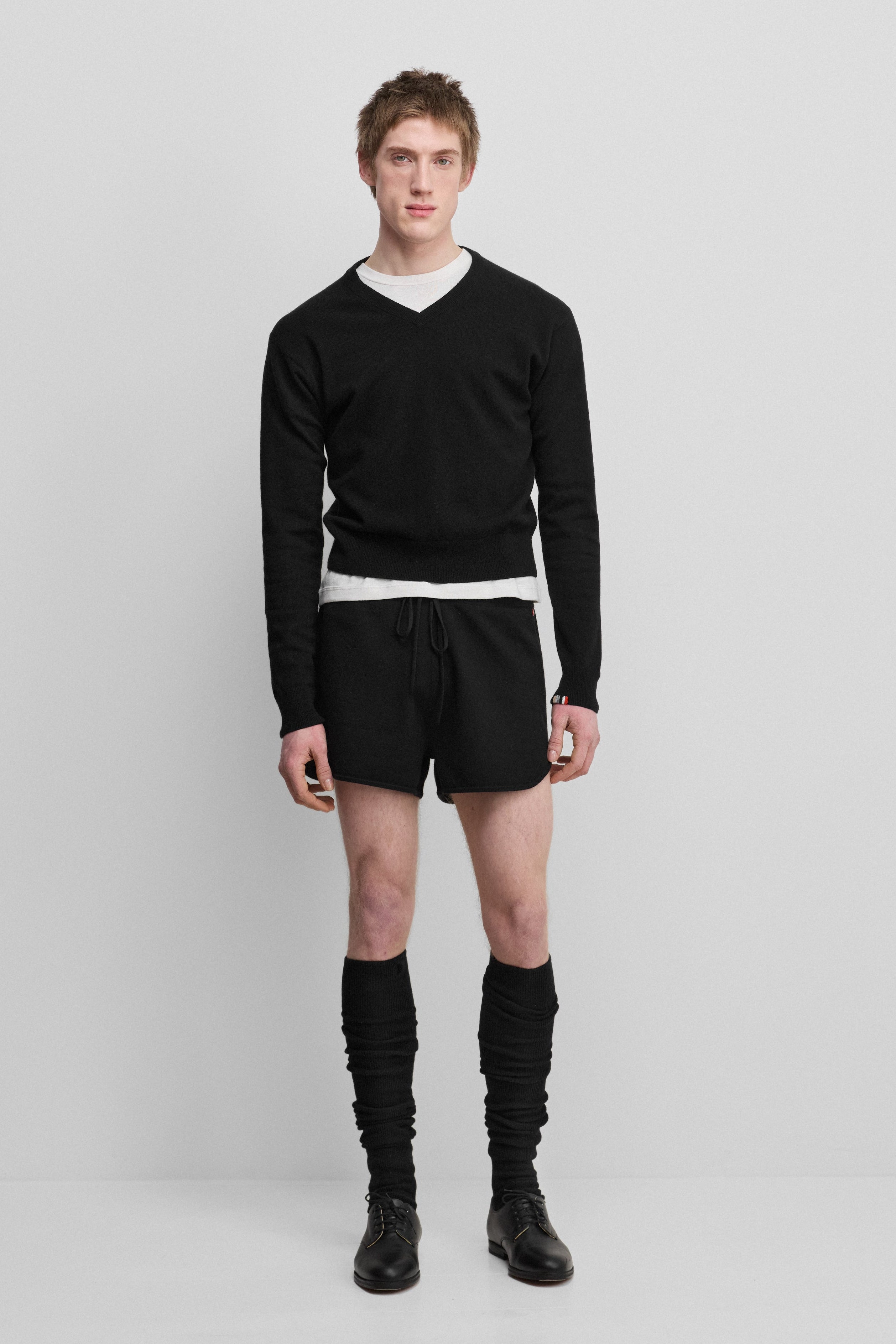 man wearing a black cashmere v-neck sweater, styled with black shorts.
