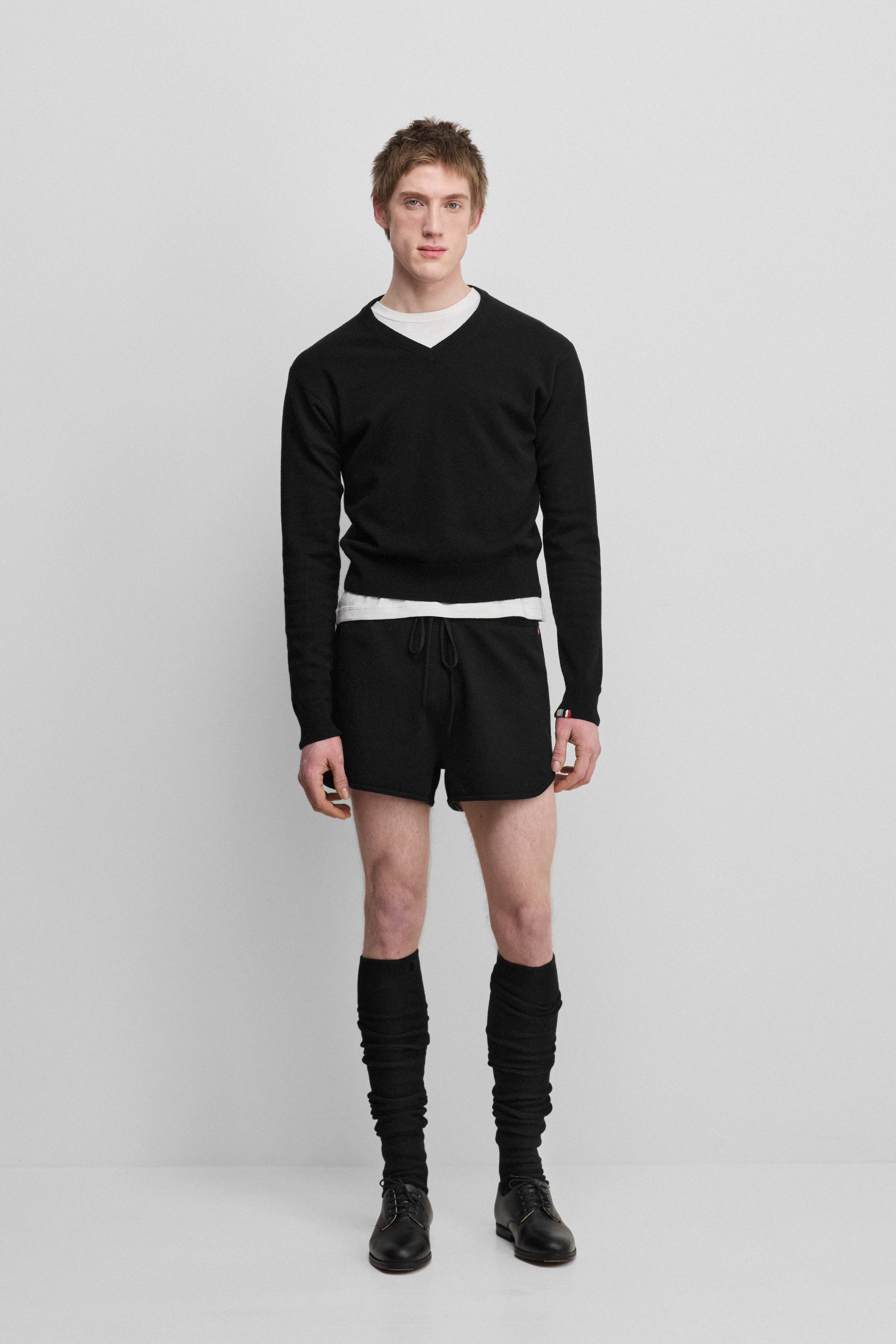 man wearing a black cashmere v-neck sweater, styled with black shorts.