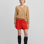 woman wearing a camel beige classic-fit cashmere v-neck sweater, styled with red shorts.