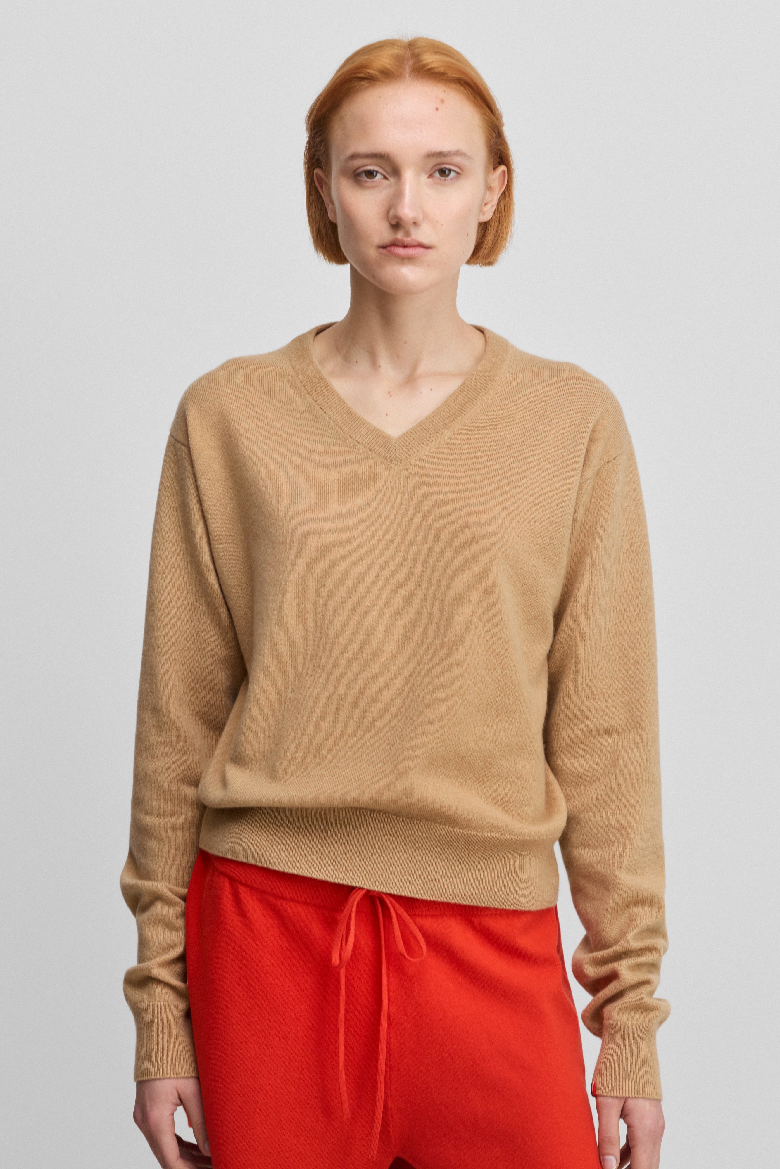 woman wearing a camel beige classic-fit cashmere v-neck sweater with ribbed trims.