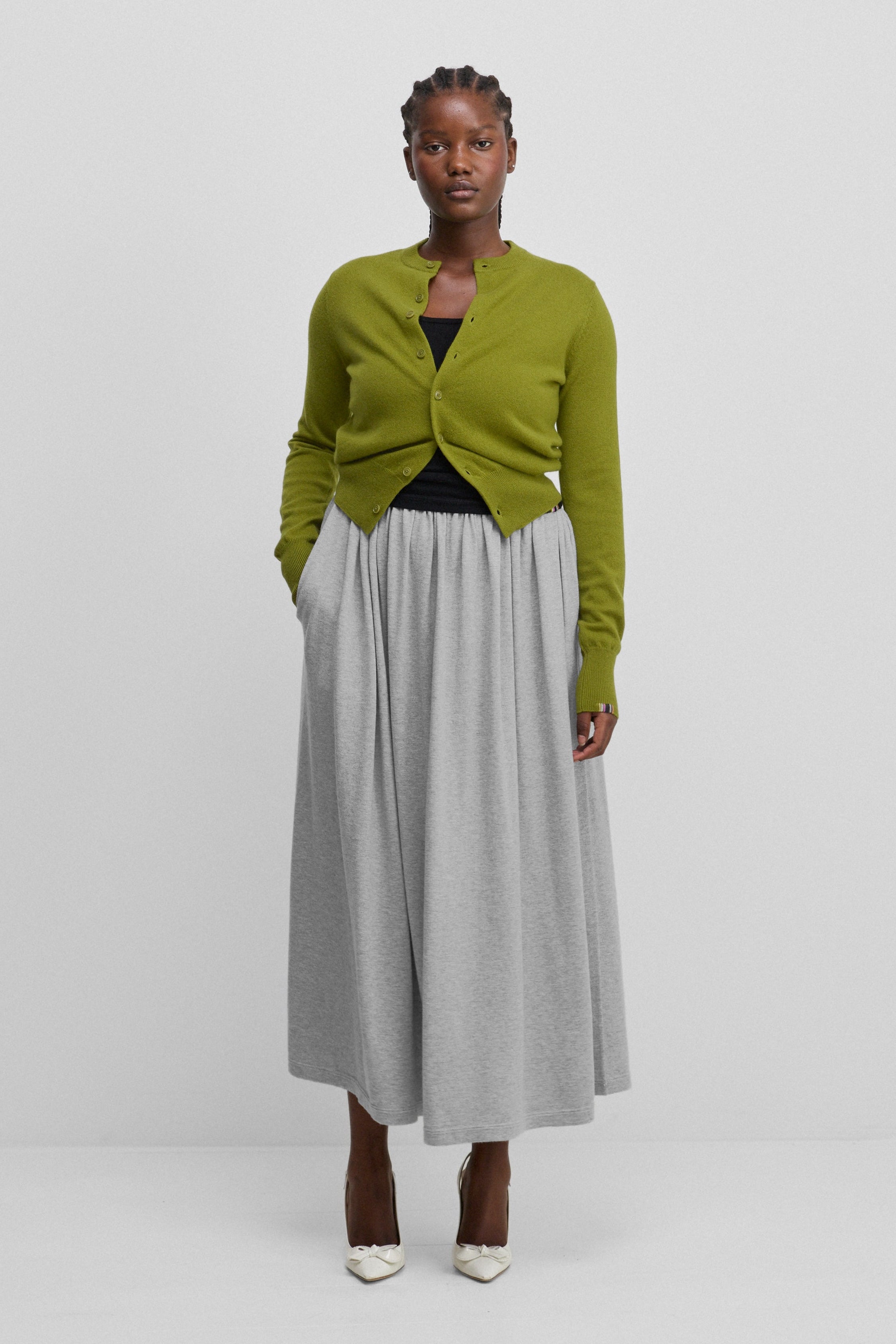 woman wearing a long grey cotton cashmere skirt with an elasticated waistband, styled with a green cardigan.