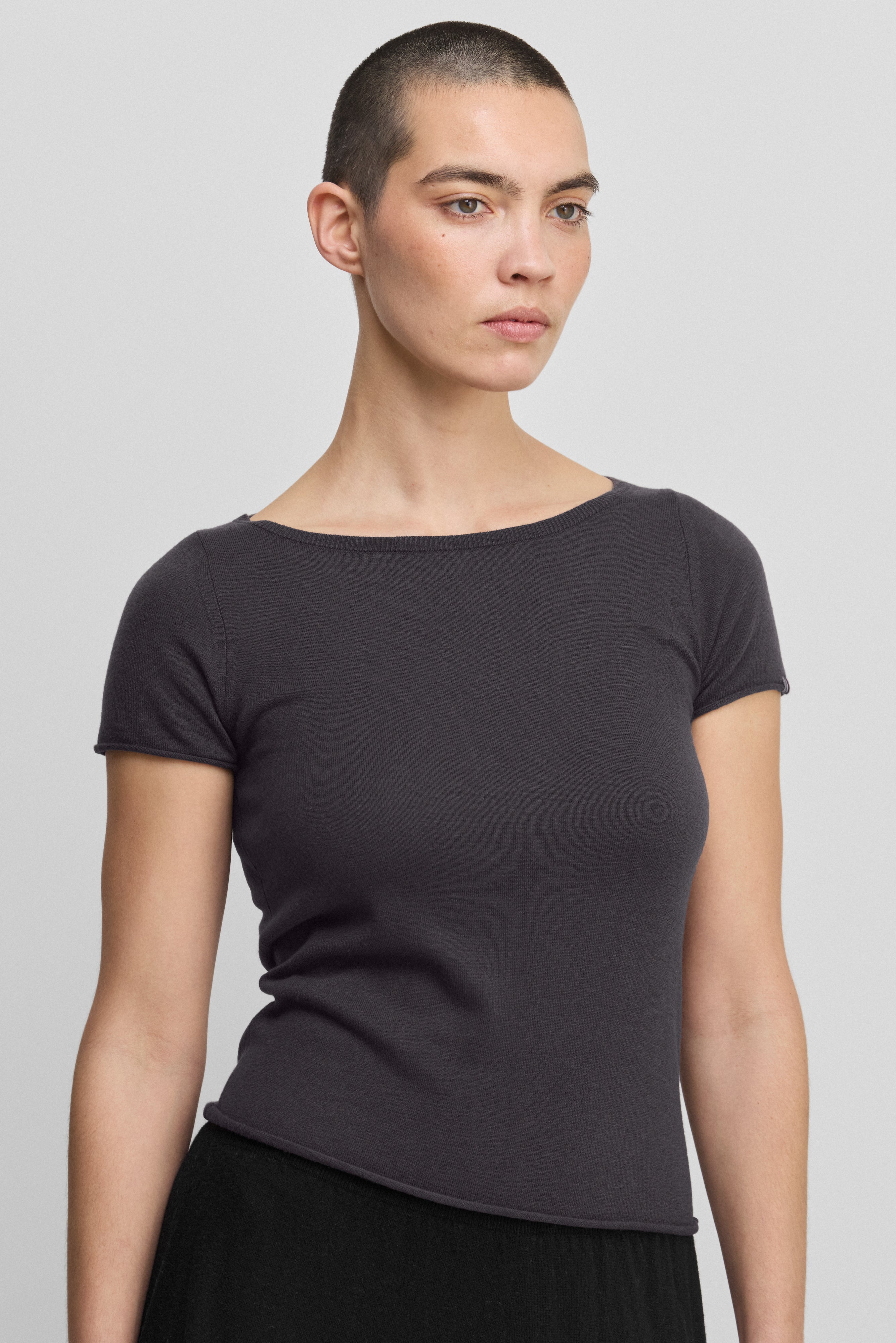 woman wearing a dark grey fitted wool cashmere t-shirt with a boat neck and rolling edge hem.