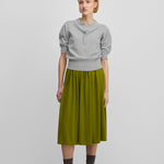woman wearing a grey half-button cashmere sweater with elbow-length sleeves, styled with a green skirt.