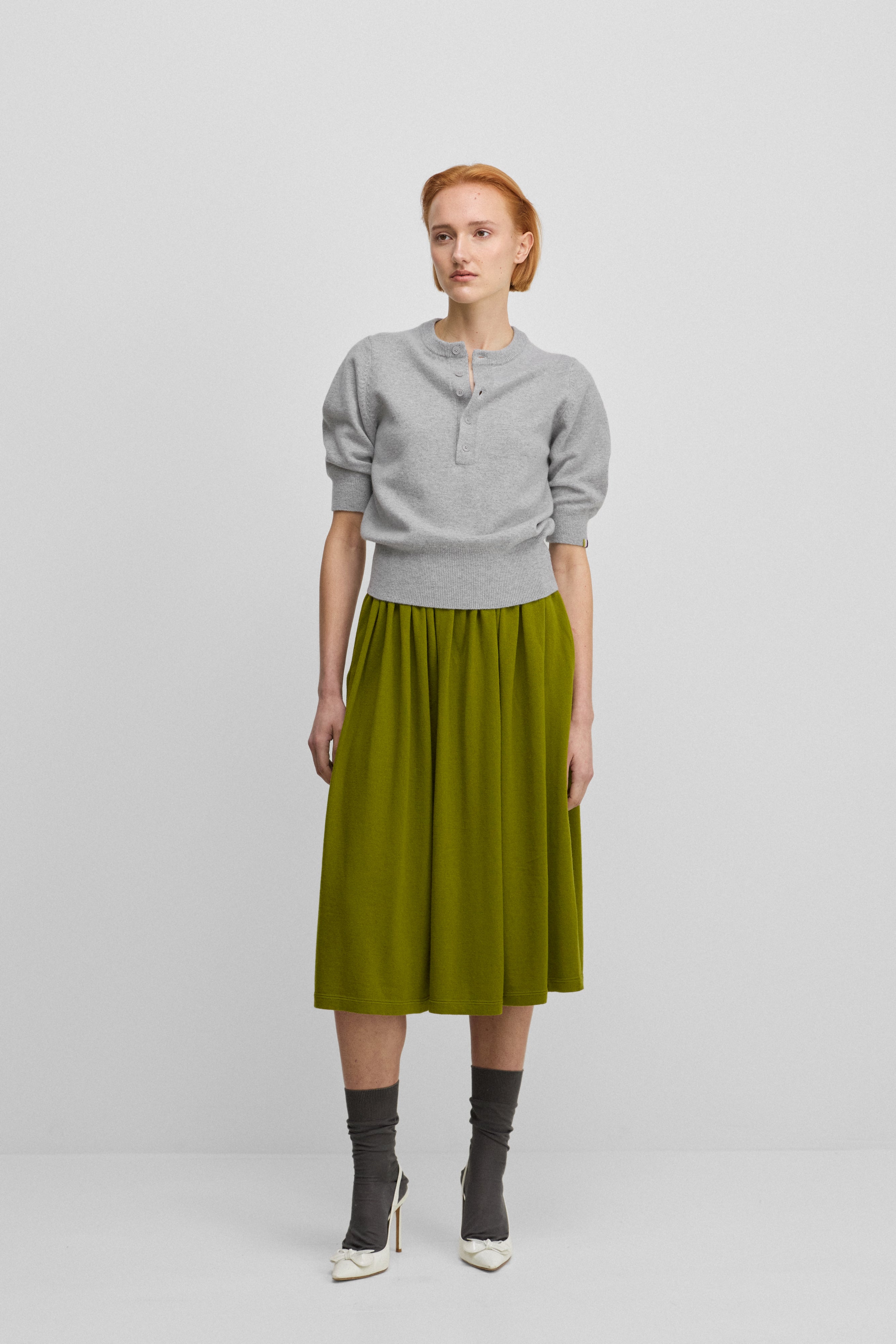 woman wearing a grey half-button cashmere sweater with elbow-length sleeves, styled with a green skirt.