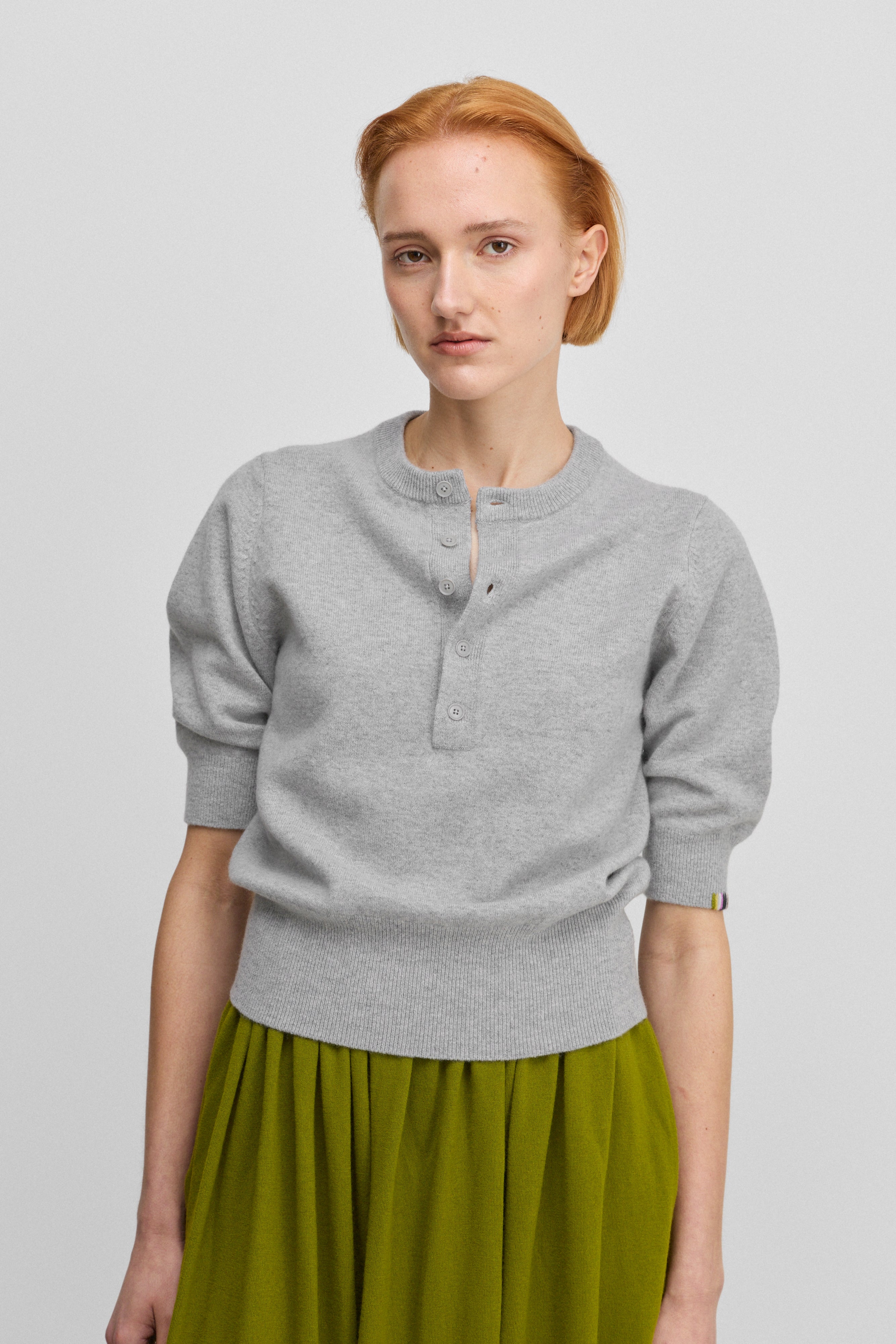 woman wearing a grey half-button cashmere sweater with elbow-length sleeves and ribbed cuffs and hem.