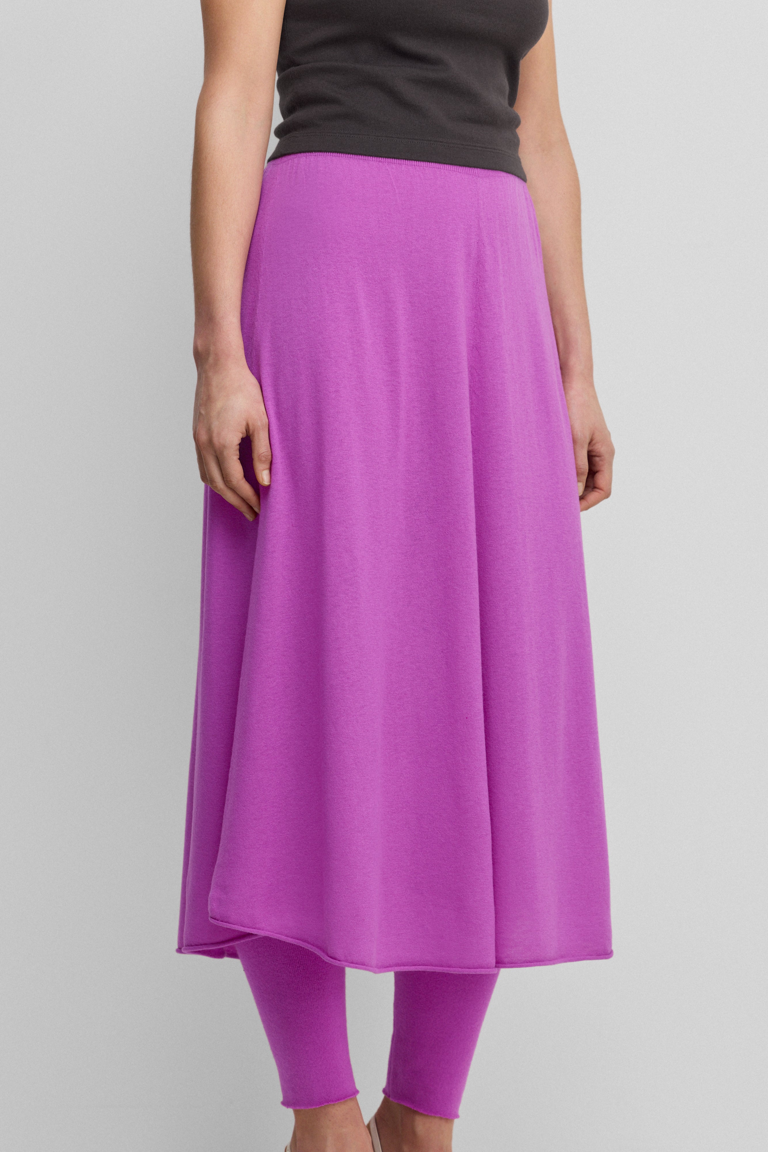 woman wearing a bright pink flared wool cashmere midi skirt with a rolling edge hem.