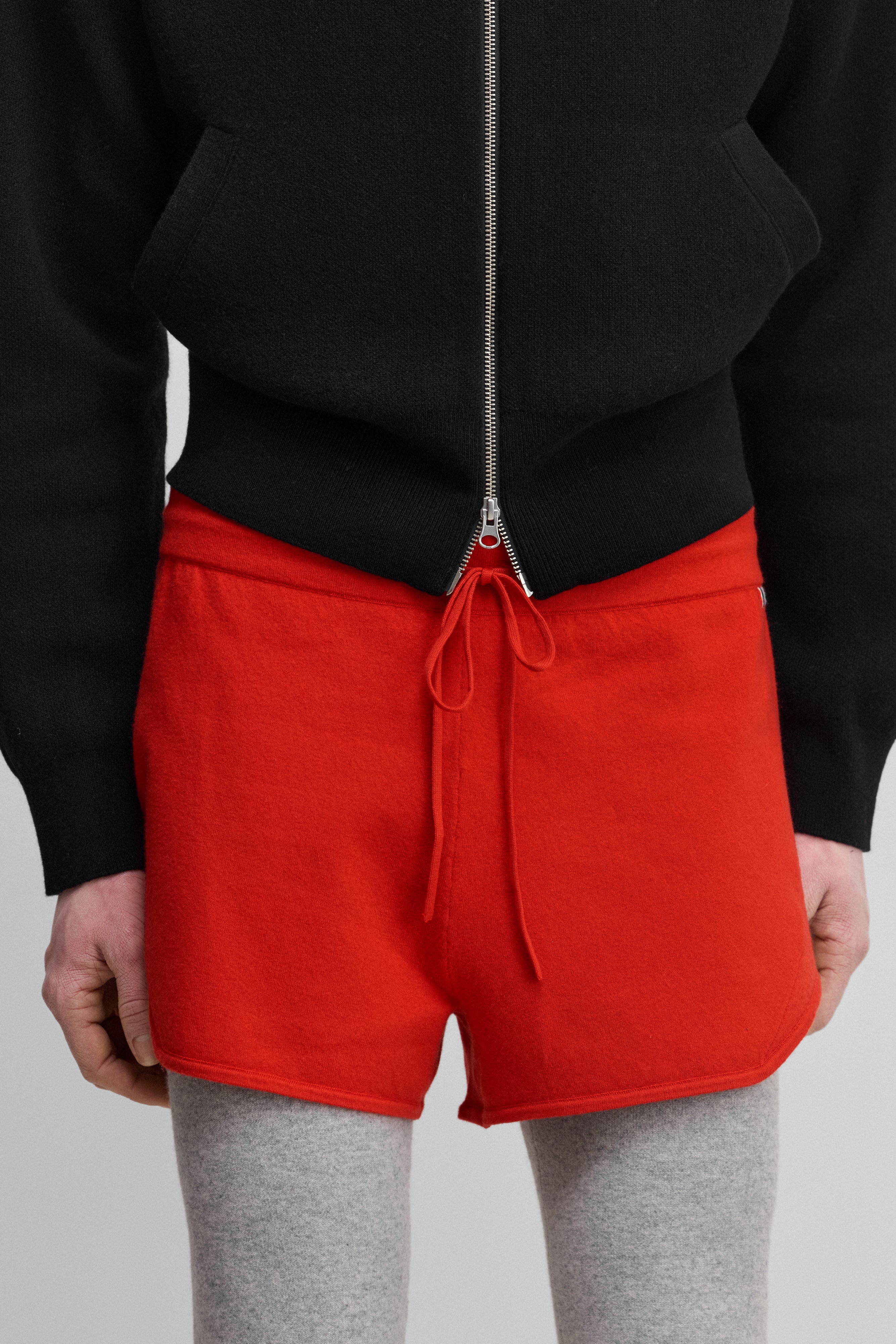 model wearing bright red cotton-cashmere mini-rib shorts with a drawstring and curved hem.