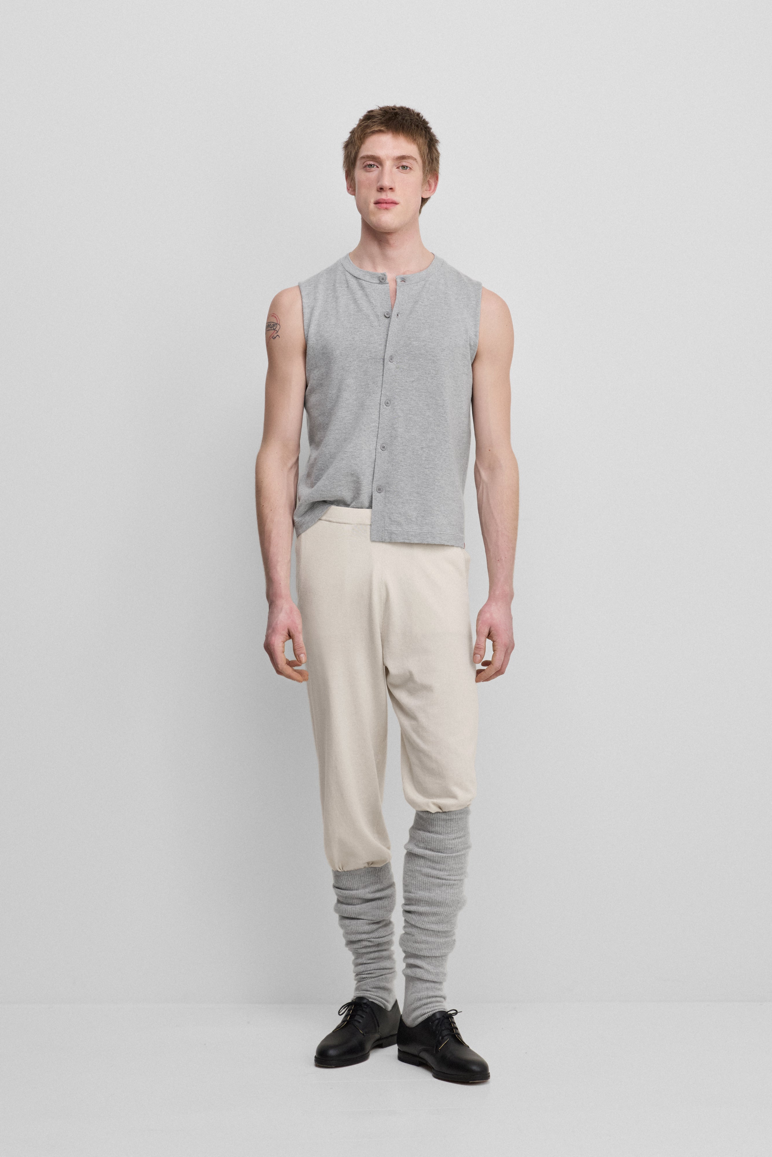 man wearing a light grey sleeveless cotton-cashmere button-up vest with a crewneck, styled with cream pants.