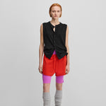 woman wearing a black sleeveless cotton-cashmere button-up vest, styled with red shorts.