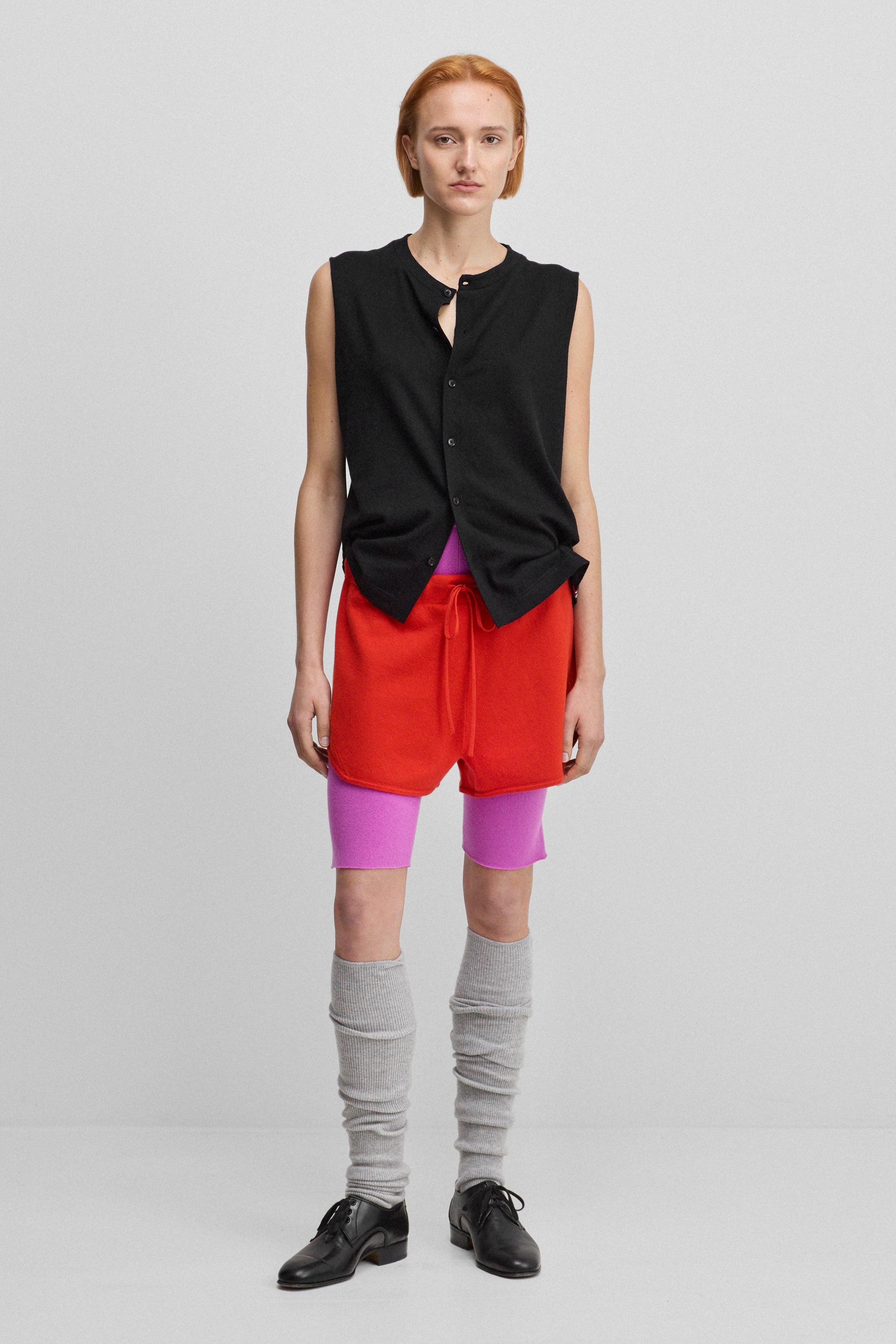 woman wearing a black sleeveless cotton-cashmere button-up vest, styled with red shorts.