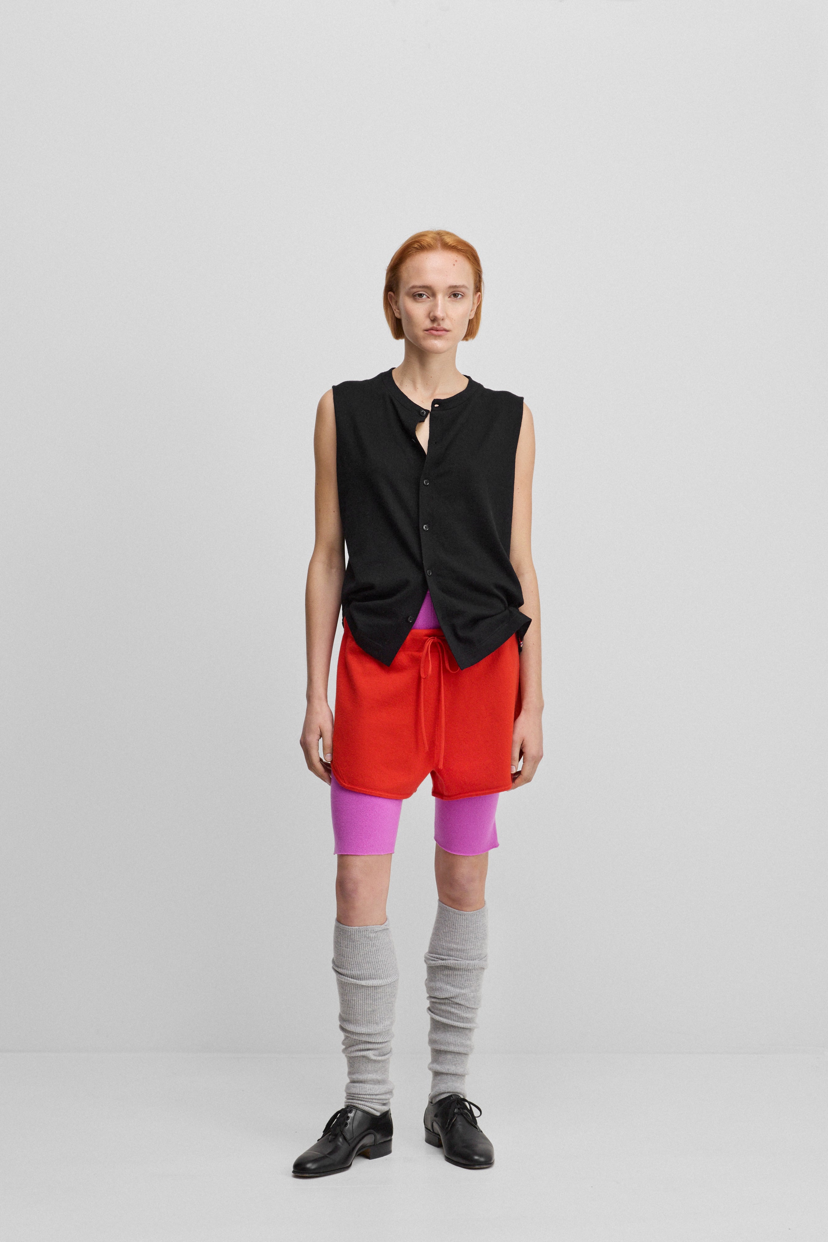 woman wearing a black sleeveless cotton-cashmere button-up vest, styled with red shorts.