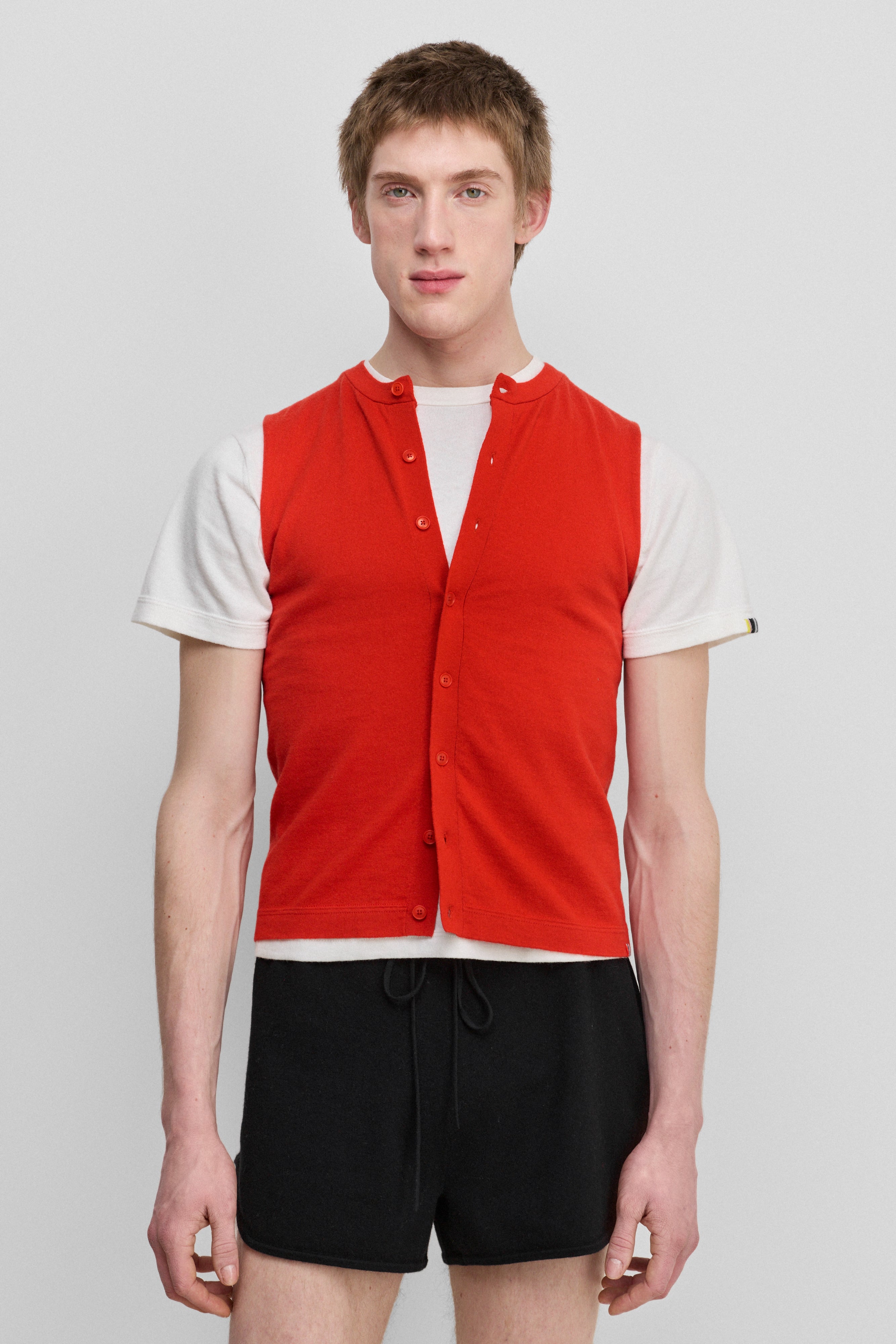 man wearing a bright red sleeveless cotton-cashmere vest with corozo buttons and a crewneck.