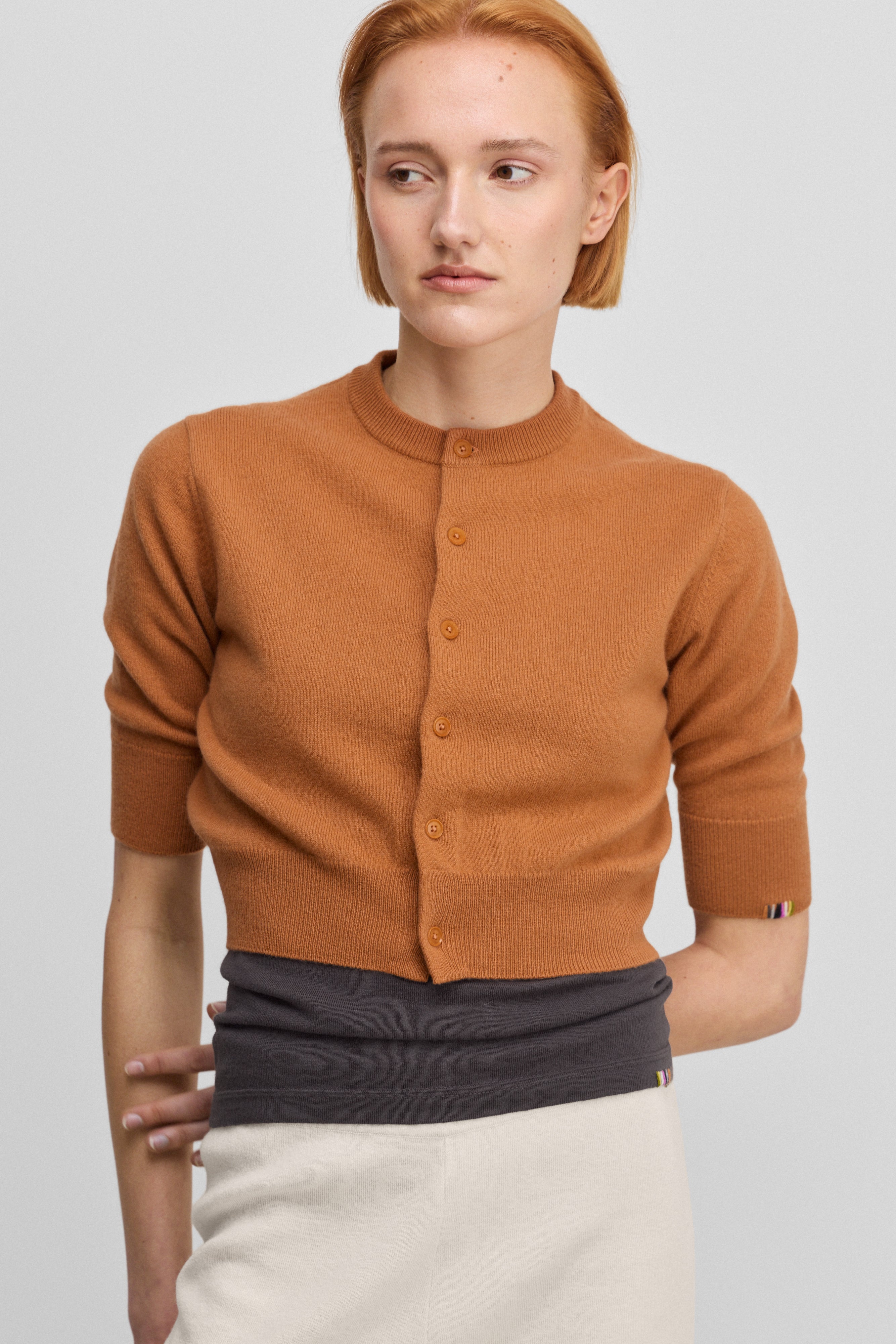 woman wearing an orange cropped button-up cardigan with elbow-length sleeves and ribbed trims.