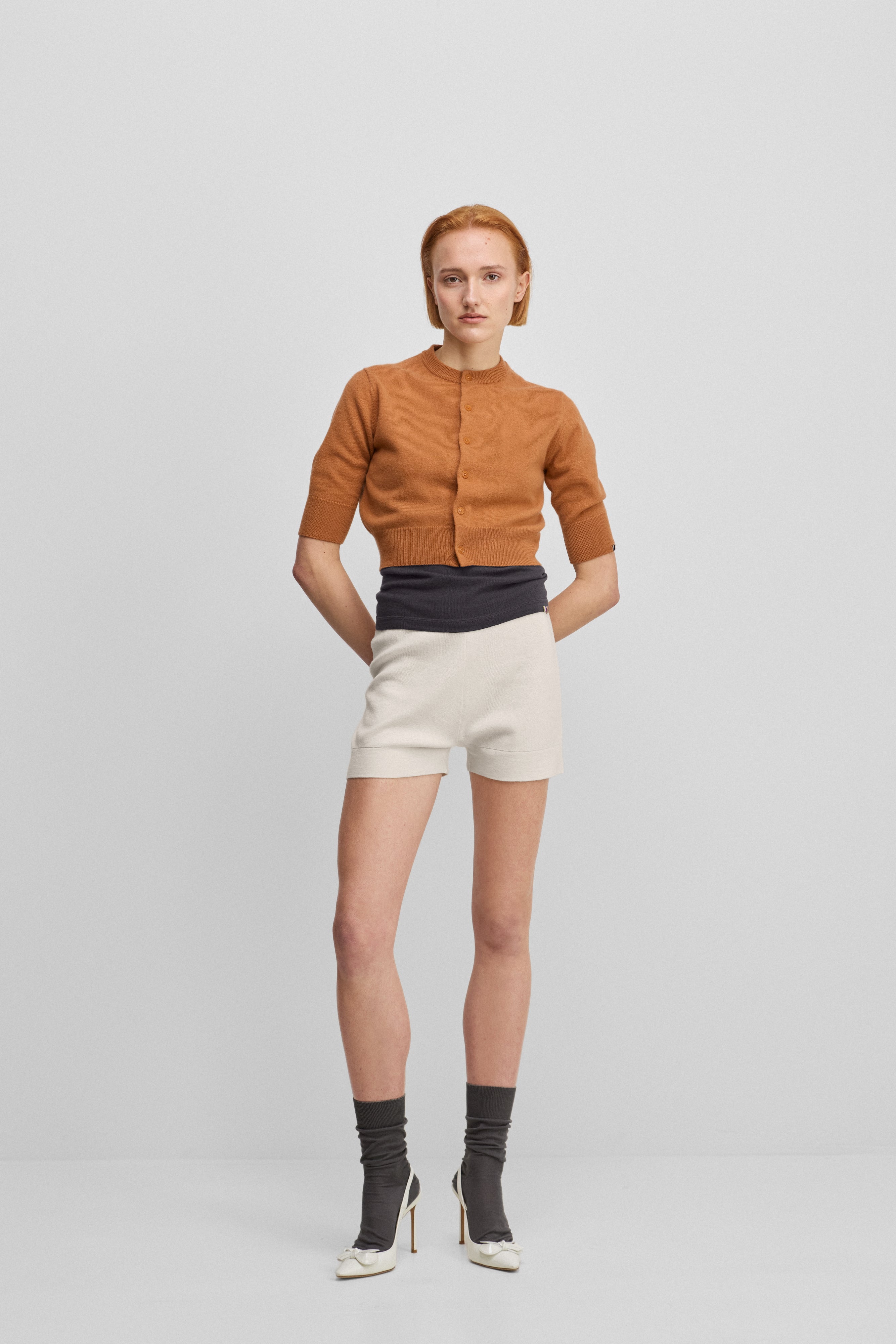 woman wearing white cotton cashmere rib-knit shorts, styled with an orange cardigan.