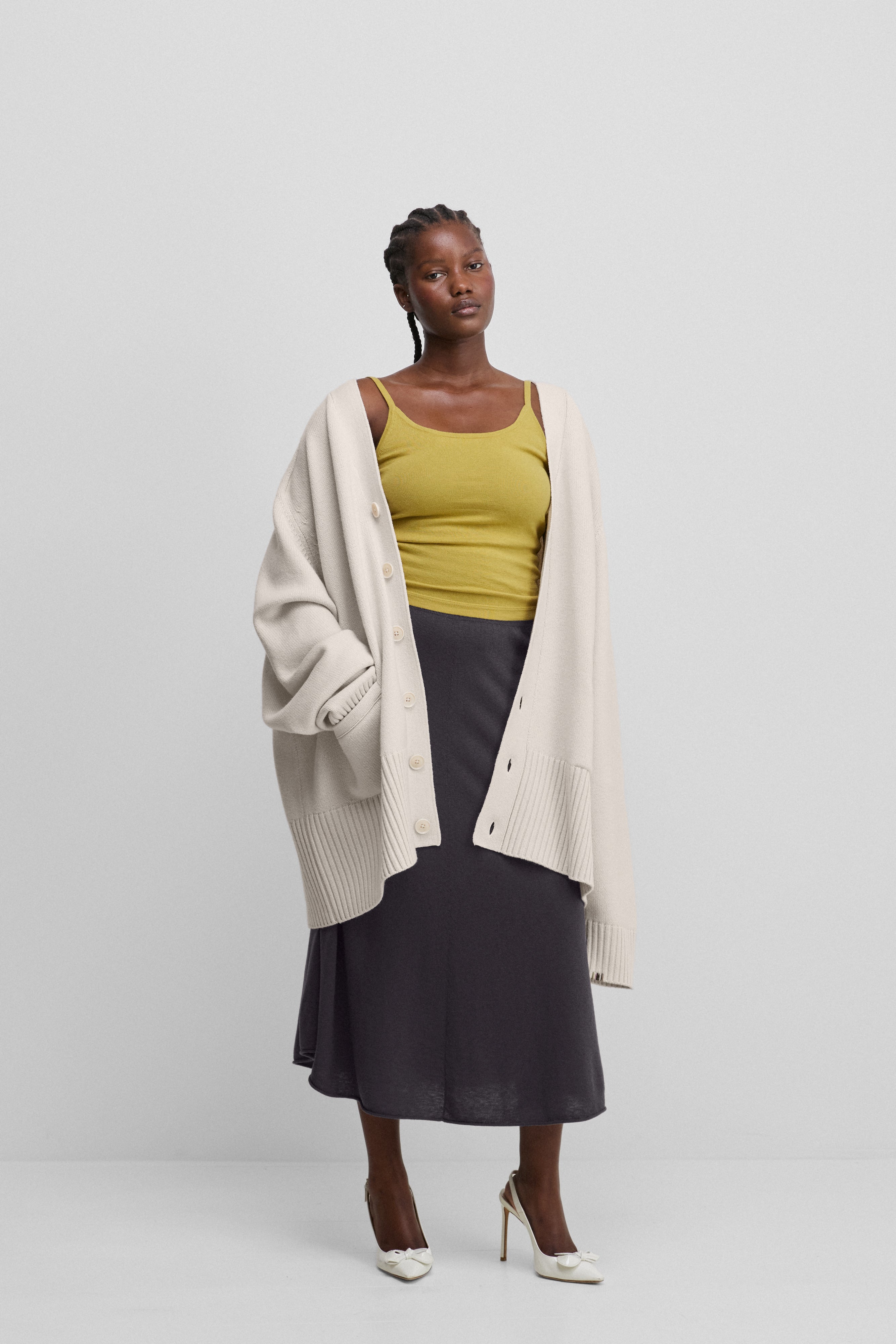 woman wearing a white oversized chunky cashmere button-up cardigan with pockets, styled with a skirt.