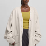 woman wearing a white oversized chunky cashmere button-up cardigan with a v-neck, pockets, ribbed trims.