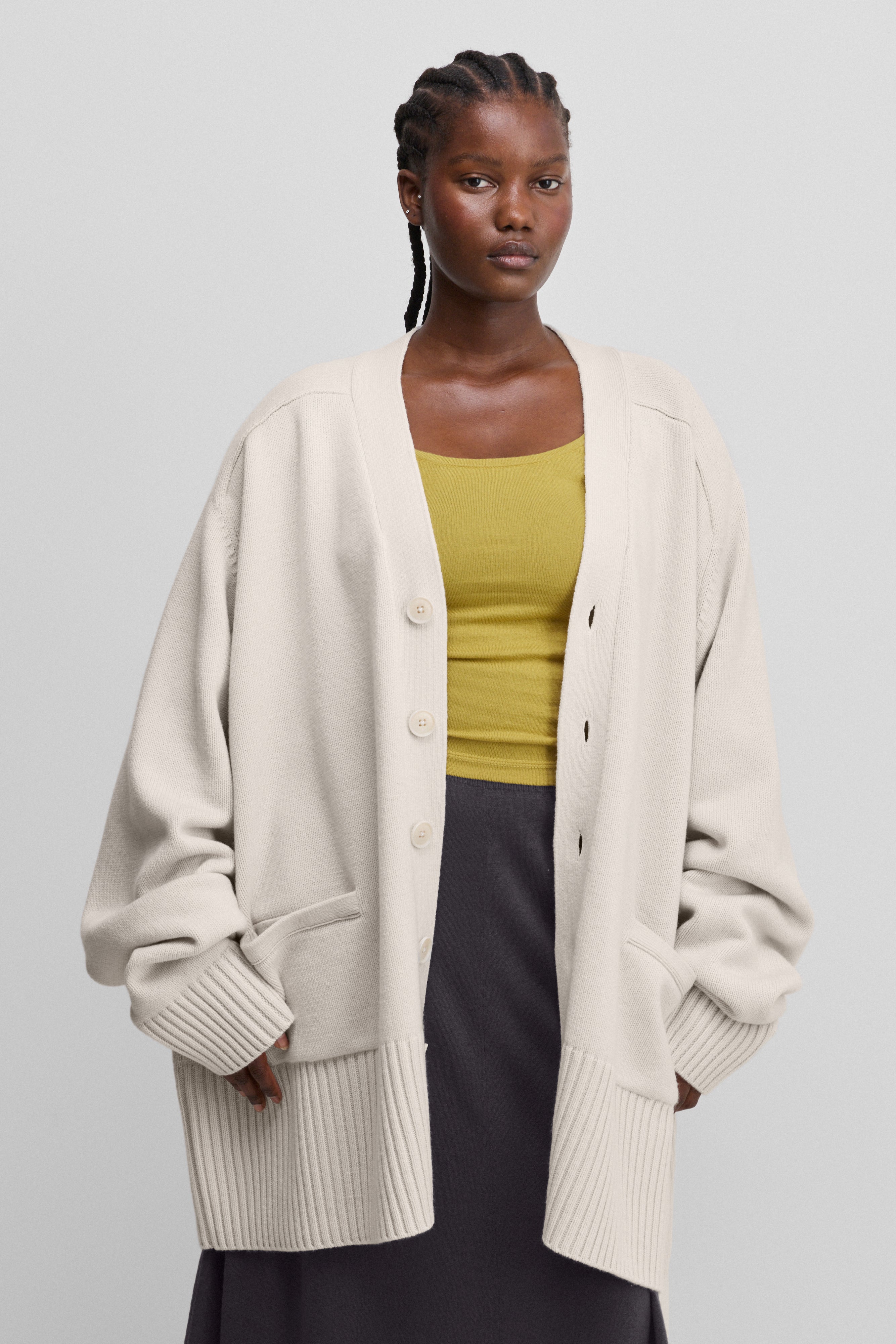 woman wearing a white oversized chunky cashmere button-up cardigan with a v-neck, pockets, ribbed trims.