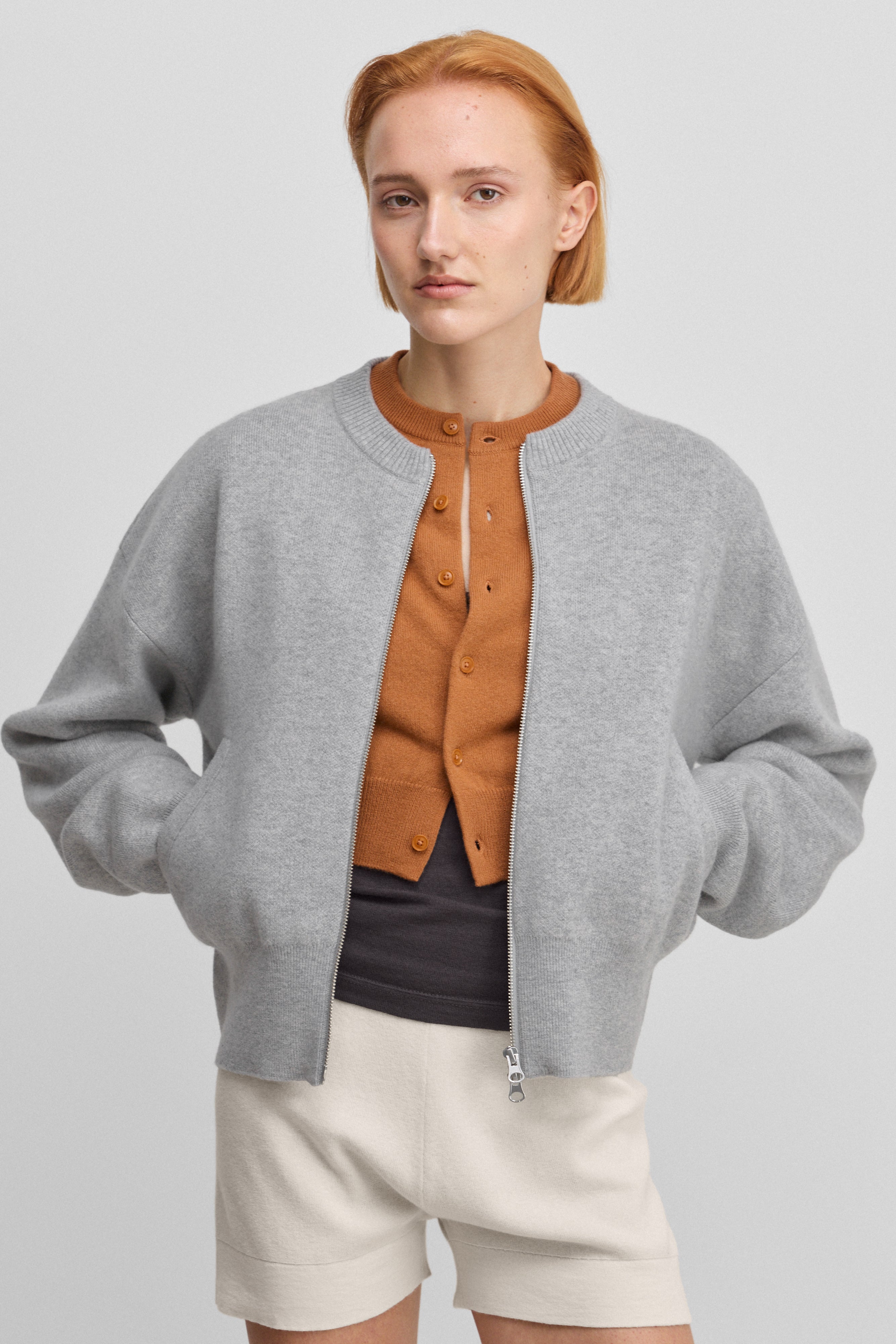 woman wearing a grey cashmere crew-neck cardigan with a metallic two-way zipper and side pockets.