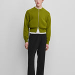 man wearing a green cropped cashmere crew-neck cardigan with a metallic two-way zipper and side pockets.