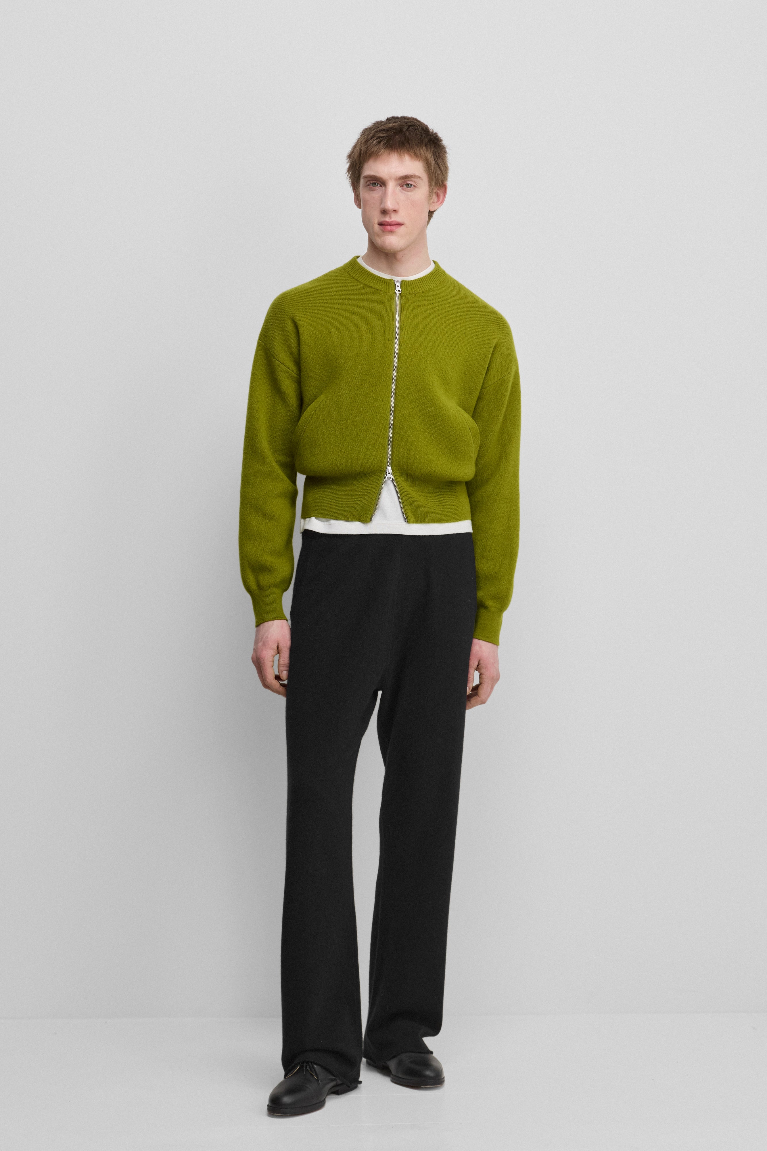 man wearing a green cropped cashmere crew-neck cardigan with a metallic two-way zipper and side pockets.