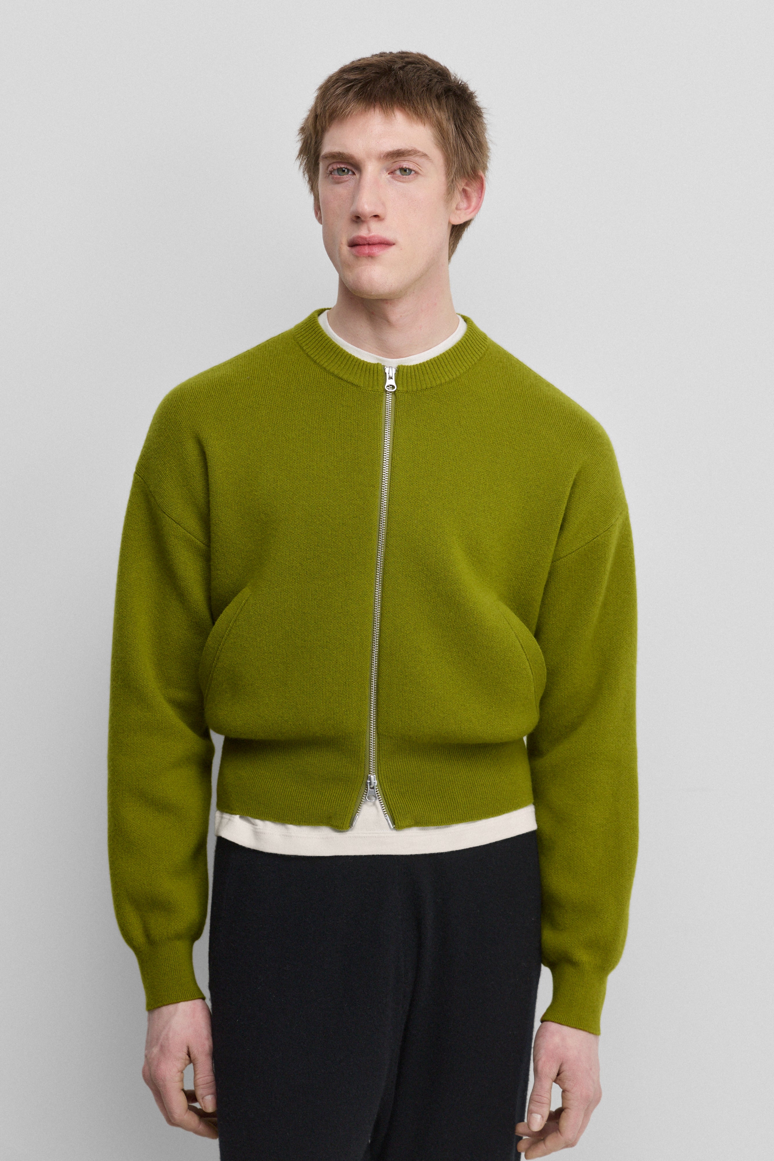 man wearing a green cashmere crew-neck cardigan with a metallic two-way zipper and two side pockets.