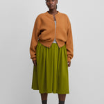 woman wearing a green cotton cashmere midi skirt, styled with an orange cardigan.