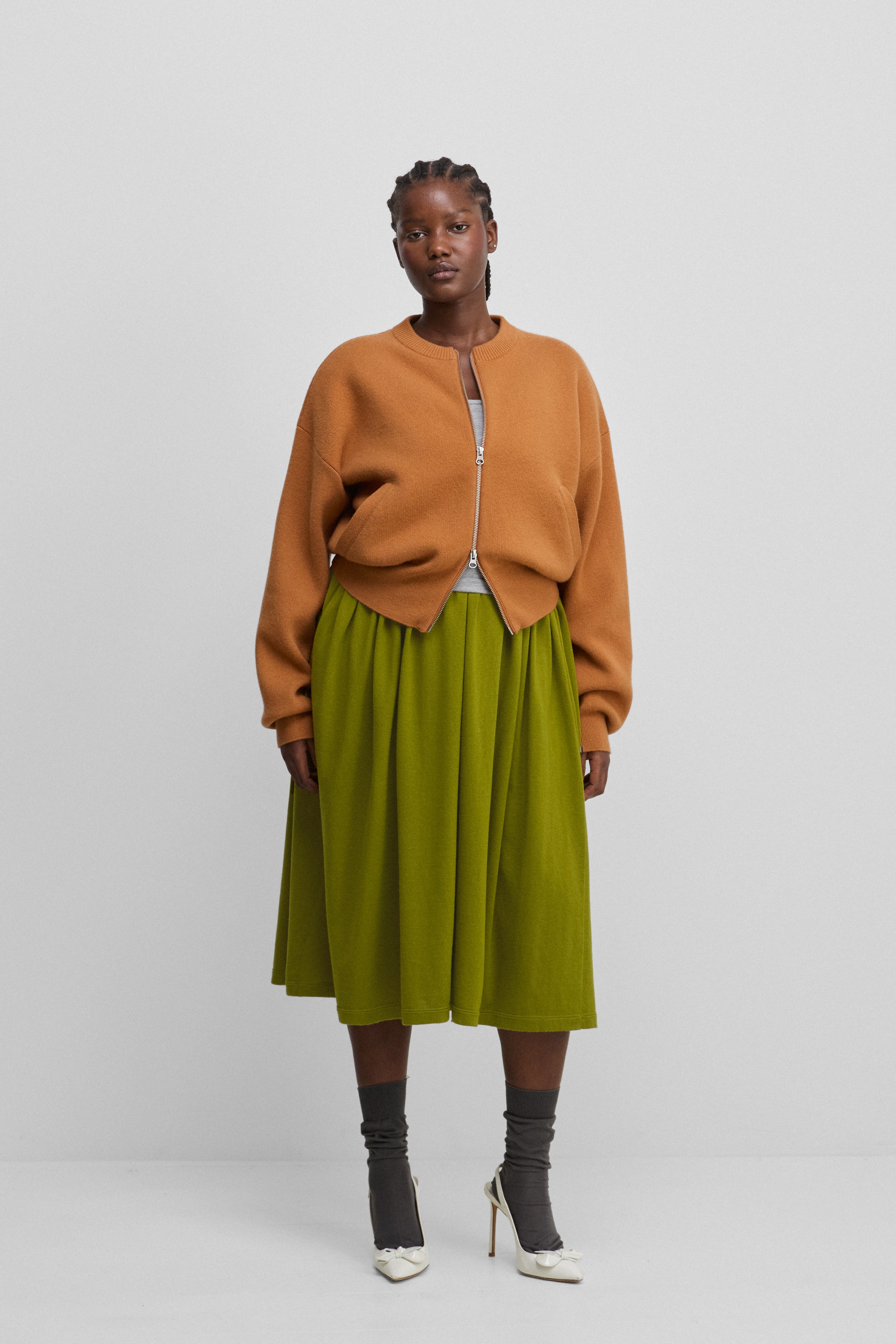 woman wearing a green cotton cashmere midi skirt, styled with an orange cardigan.