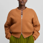 woman wearing an orange zip-up cashmere cardigan with a ribbed crew neck and two side pockets.