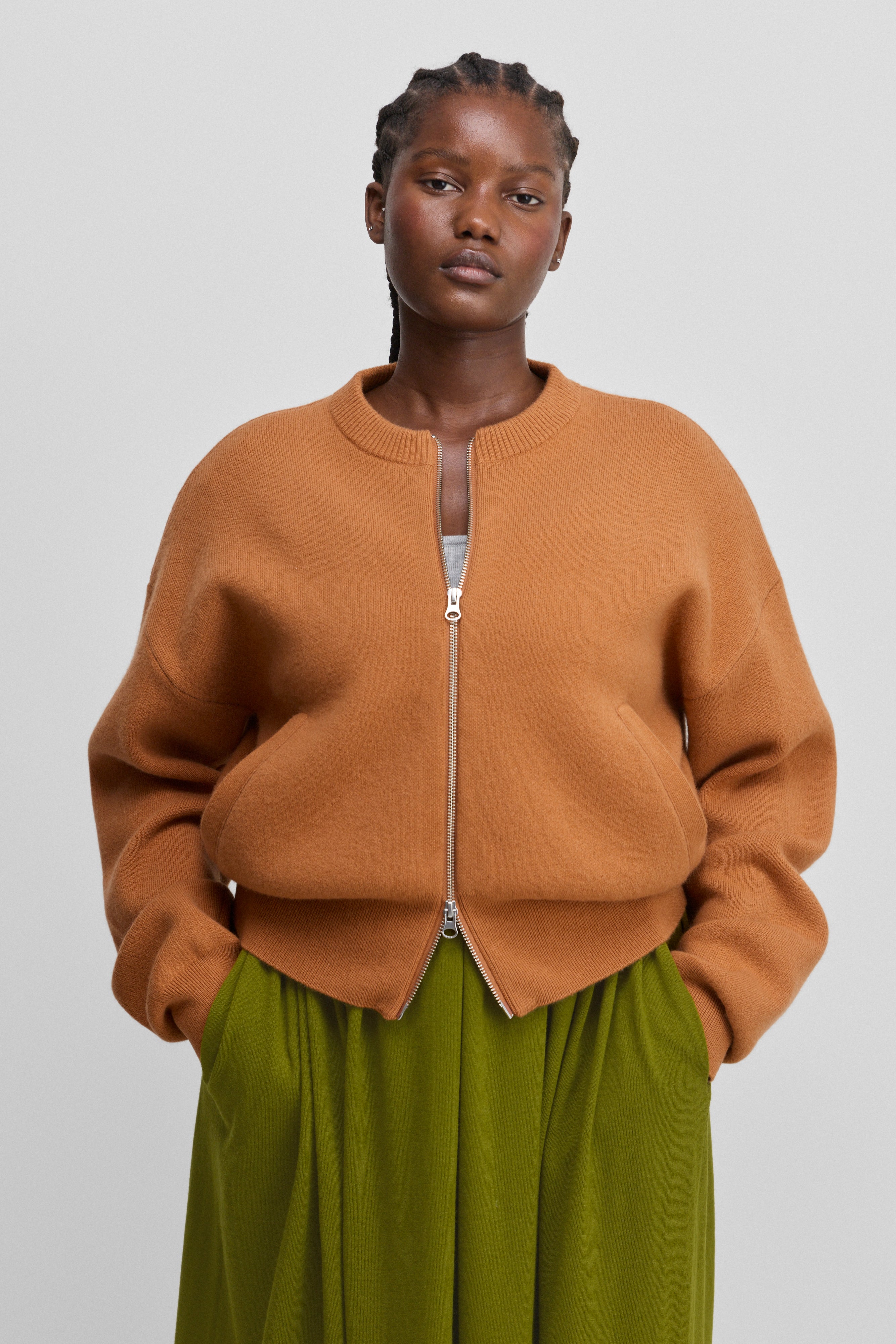 woman wearing an orange zip-up cashmere cardigan with a ribbed crew neck and two side pockets.