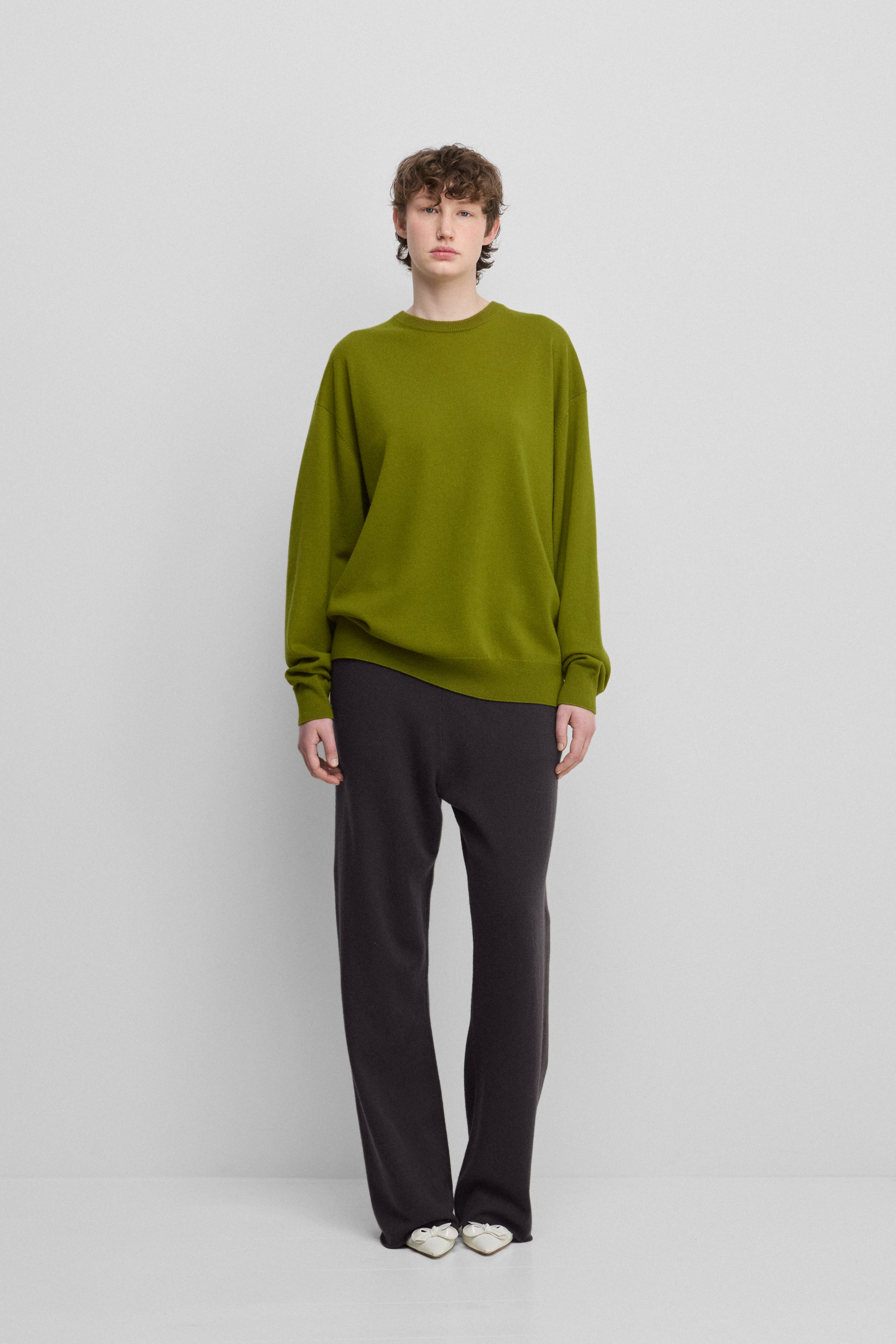 woman wearing a green loose-fit cashmere crew-neck sweater, styled with black pants.