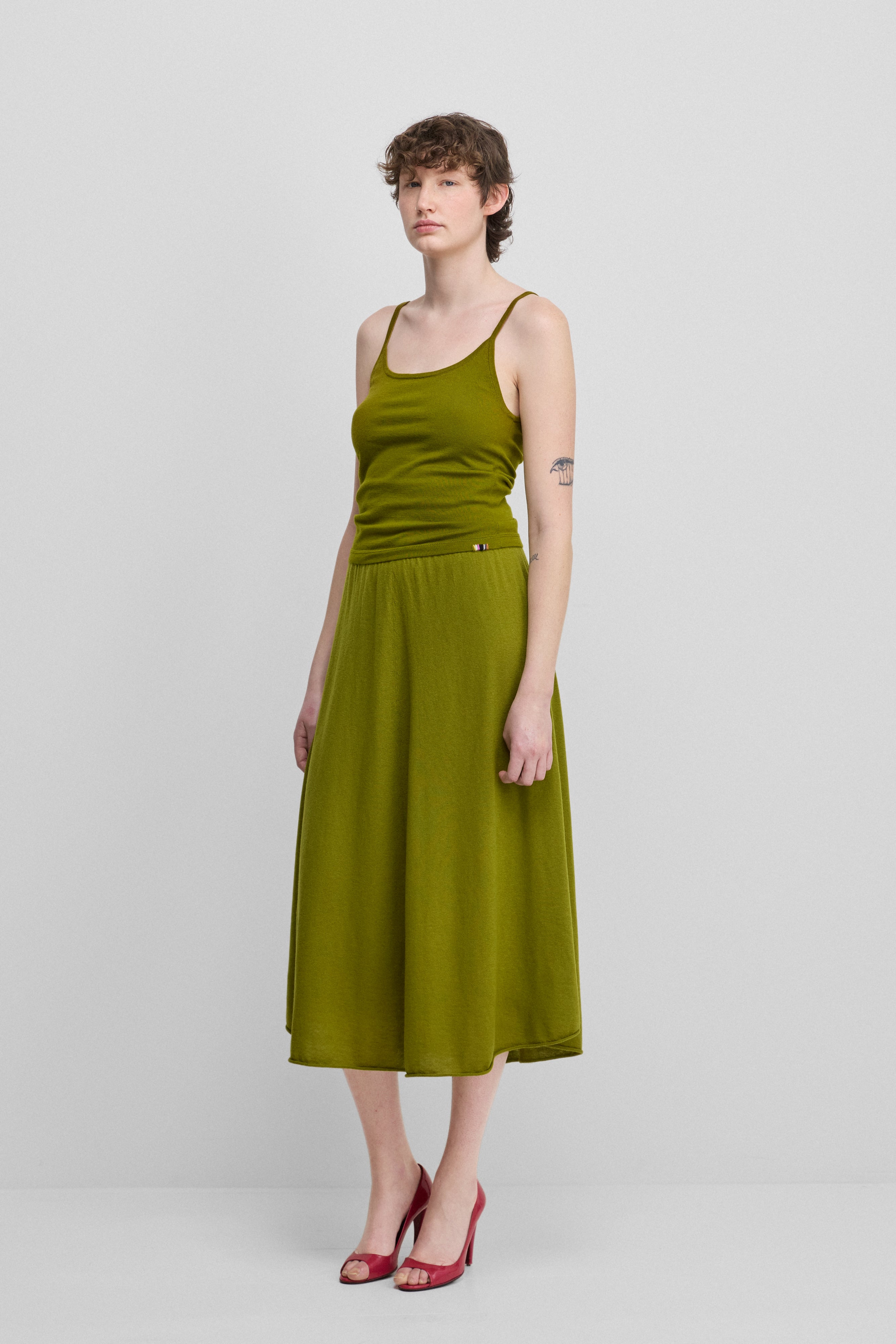woman wearing a green cotton cashmere strap top with a round neckline, styled with a green skirt.